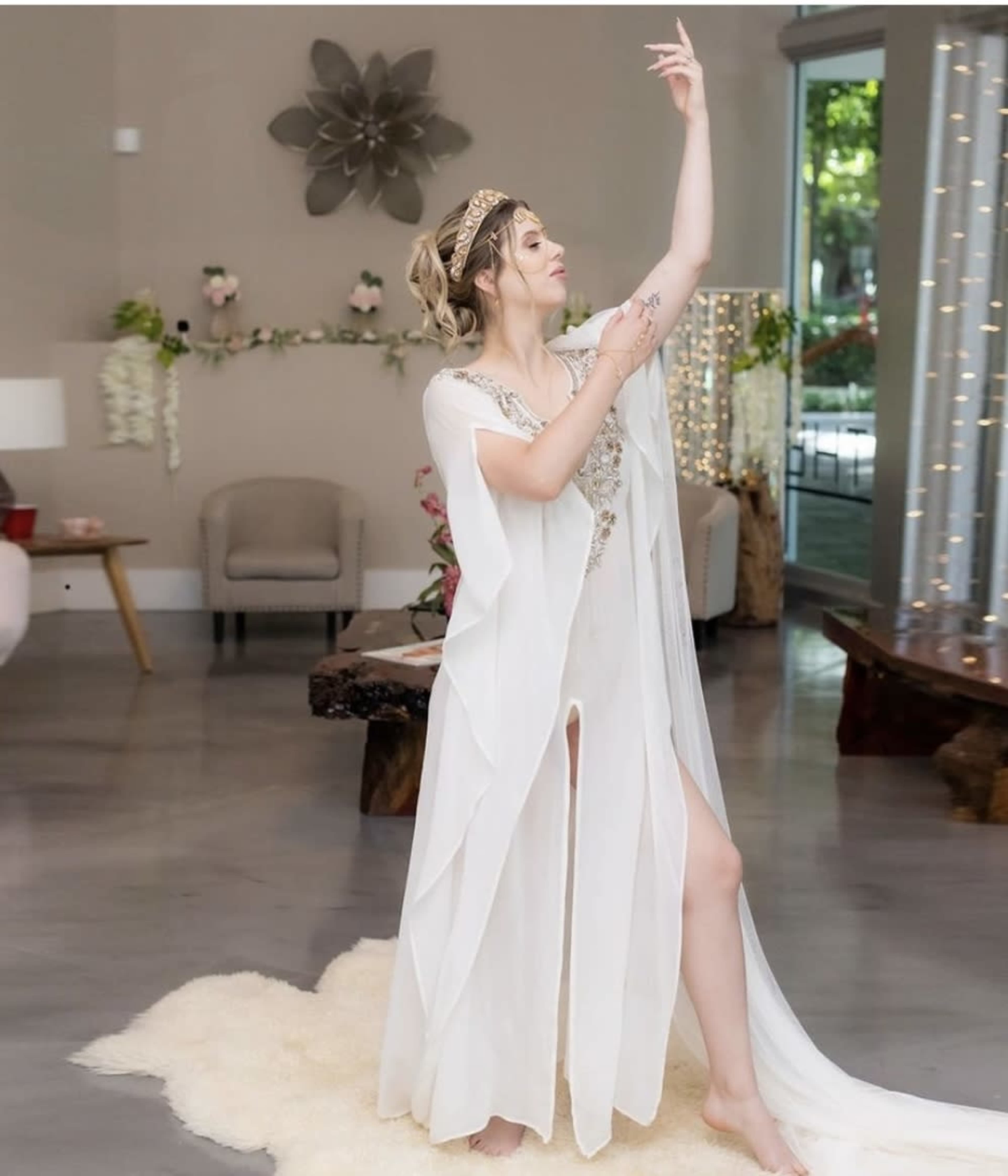 A person in a flowing white garment poses gracefully in an elegantly decorated indoor space.