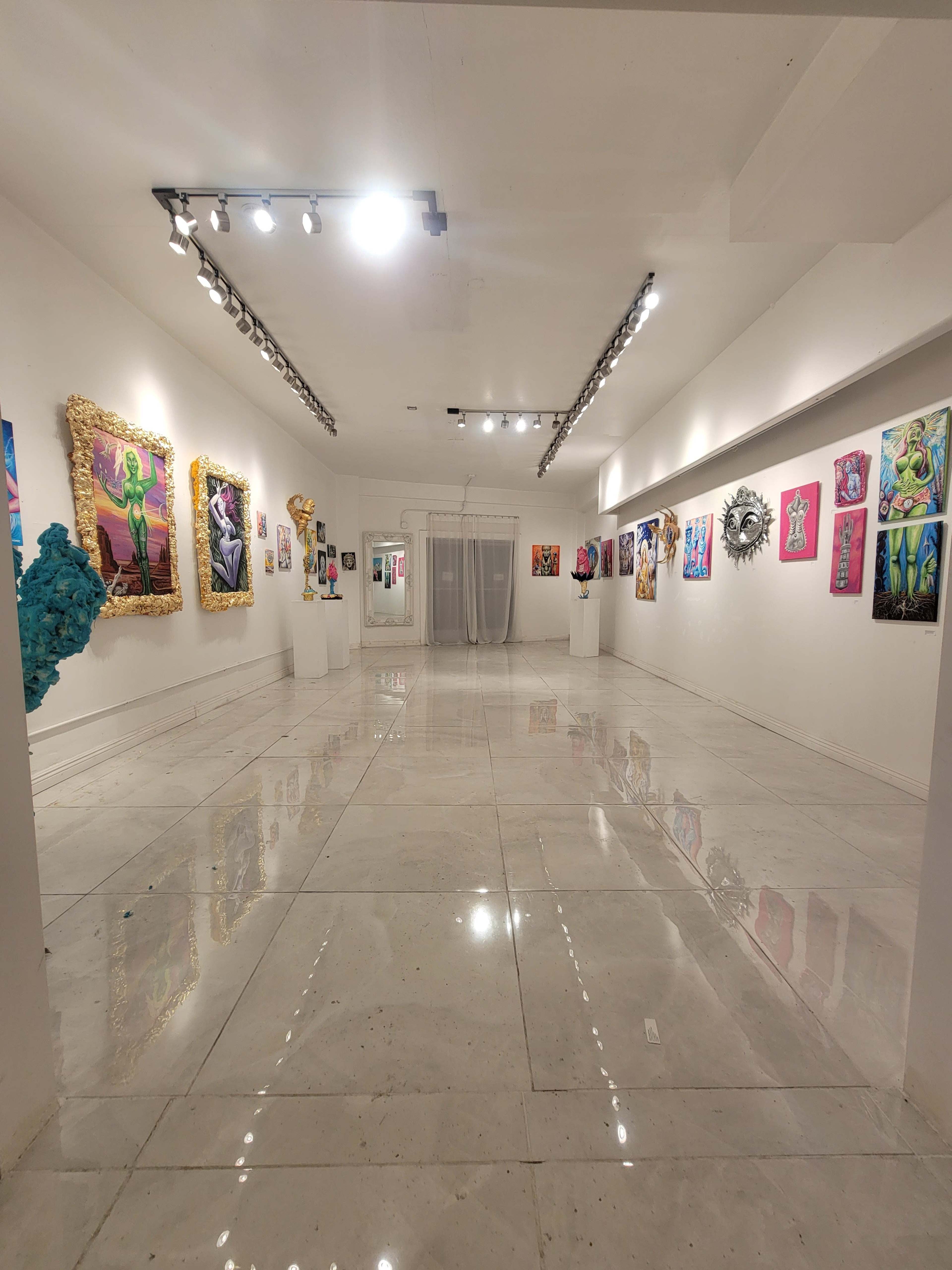 A modern art gallery with white walls, polished floors, and various colorful artworks displayed on the walls and on pedestals.