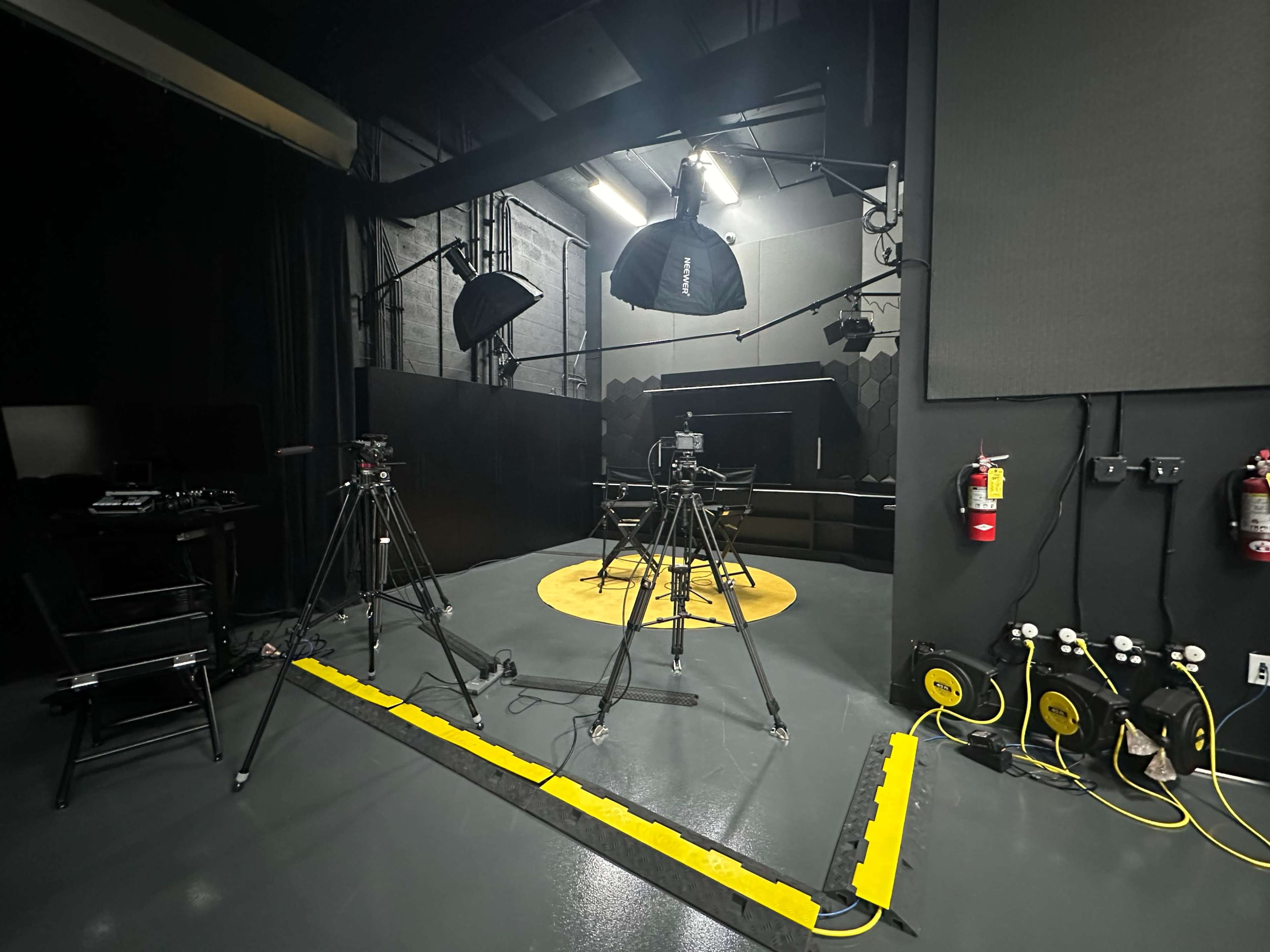 A video production studio is equipped with multiple cameras and lighting setups, featuring a circular yellow stage area.