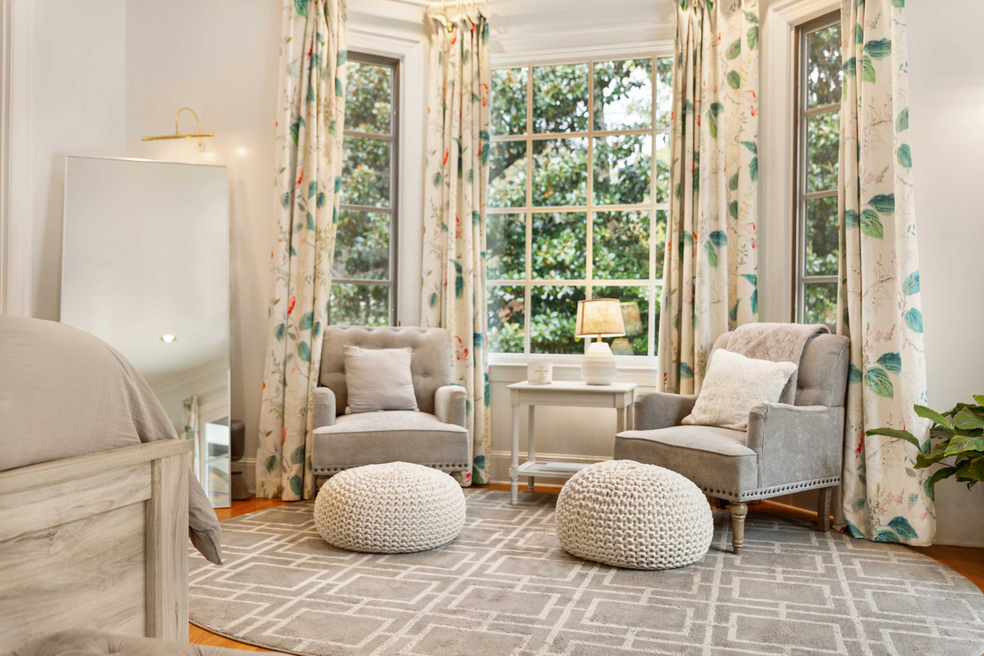 A bright room with two armchairs, a small table, decorative curtains, and a large mirror.