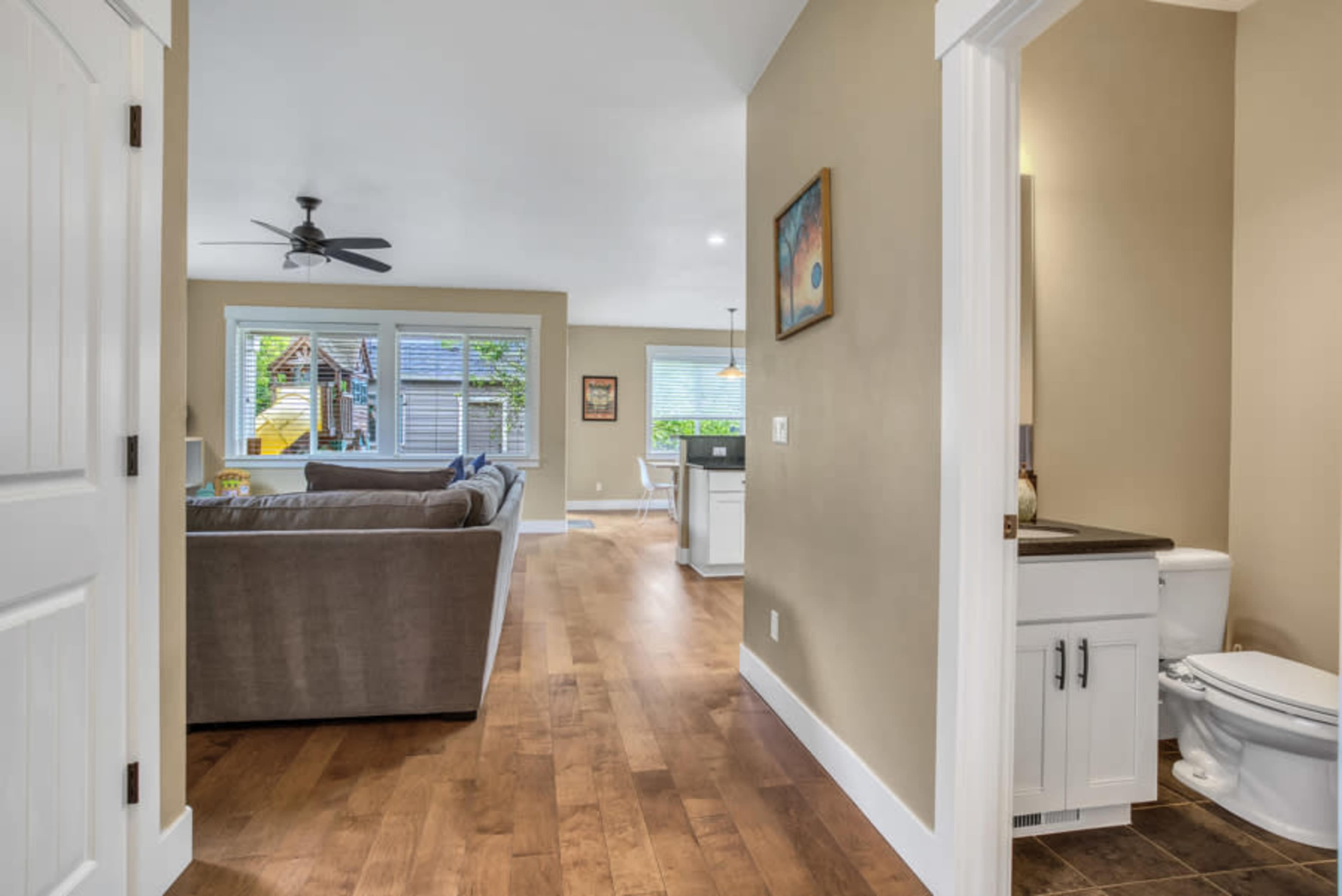 A view from a hallway into a bright living area with a sofa, dining space, and a small bathroom on the left.