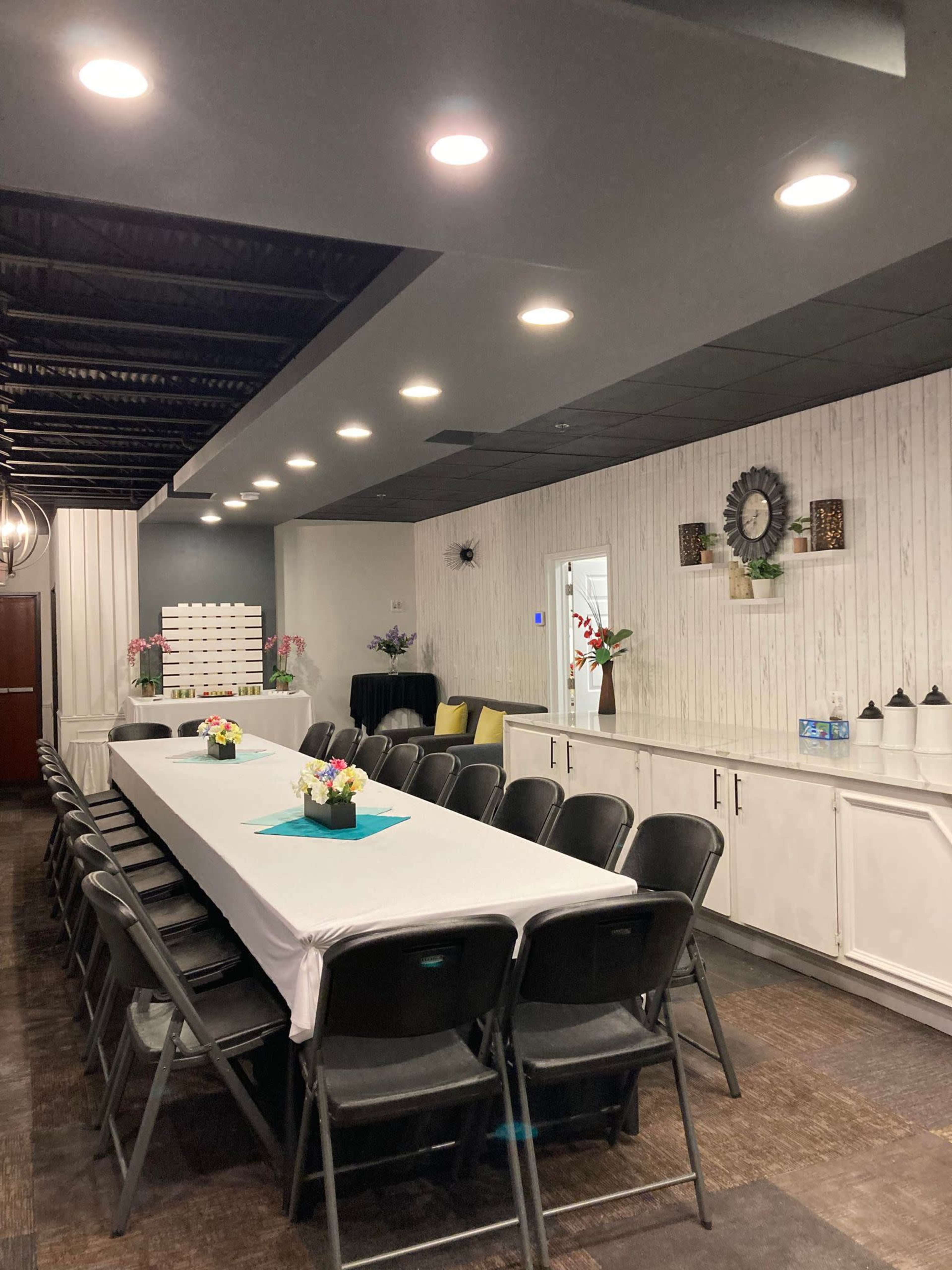 A modern meeting room featuring a long table with black chairs, decorative plants, and wall-mounted shelves.