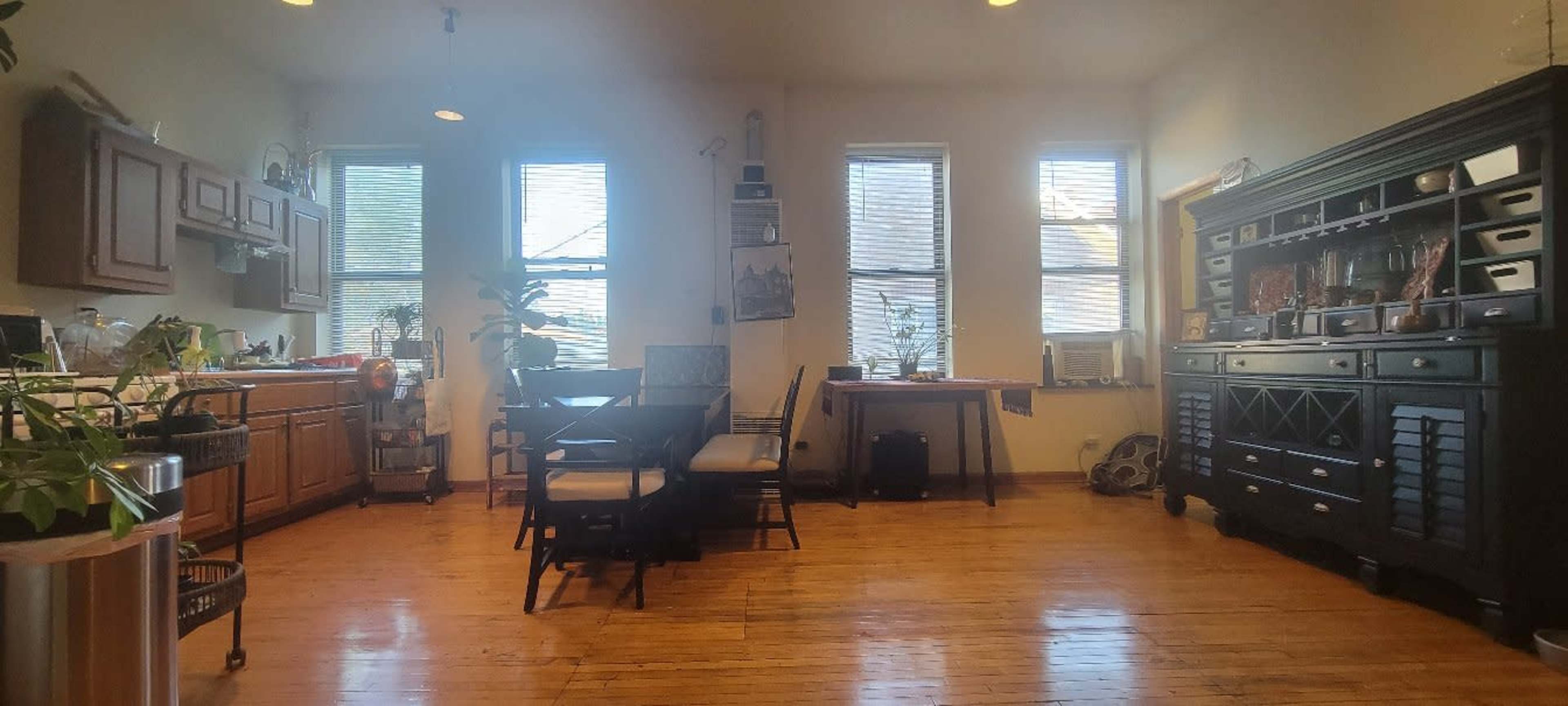 A kitchen and dining area with wooden floors, a table and chairs, and cabinets along the walls.