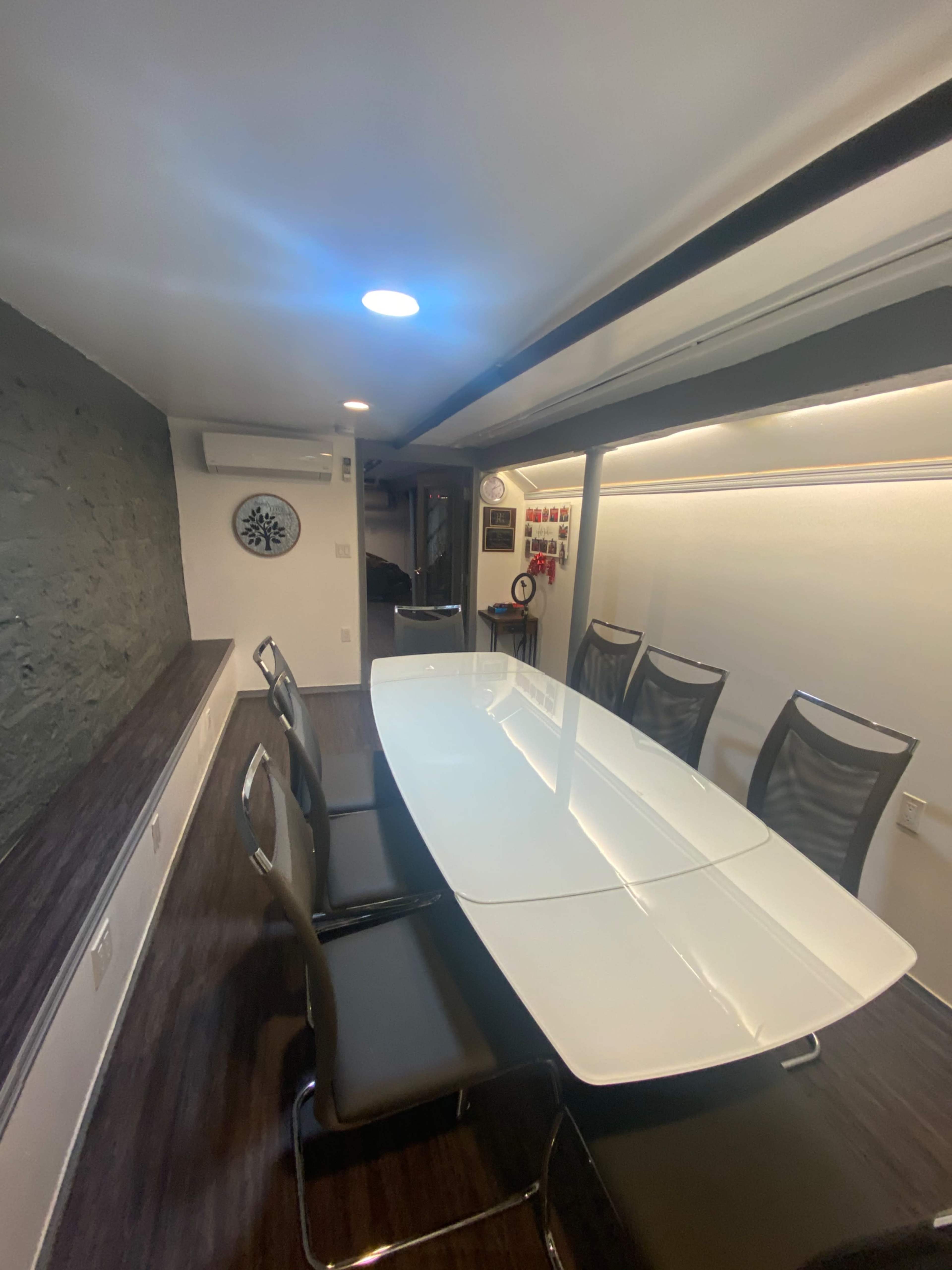 A modern conference room with a glossy white table surrounded by black chairs, featuring a gray stone wall and ceiling lights.
