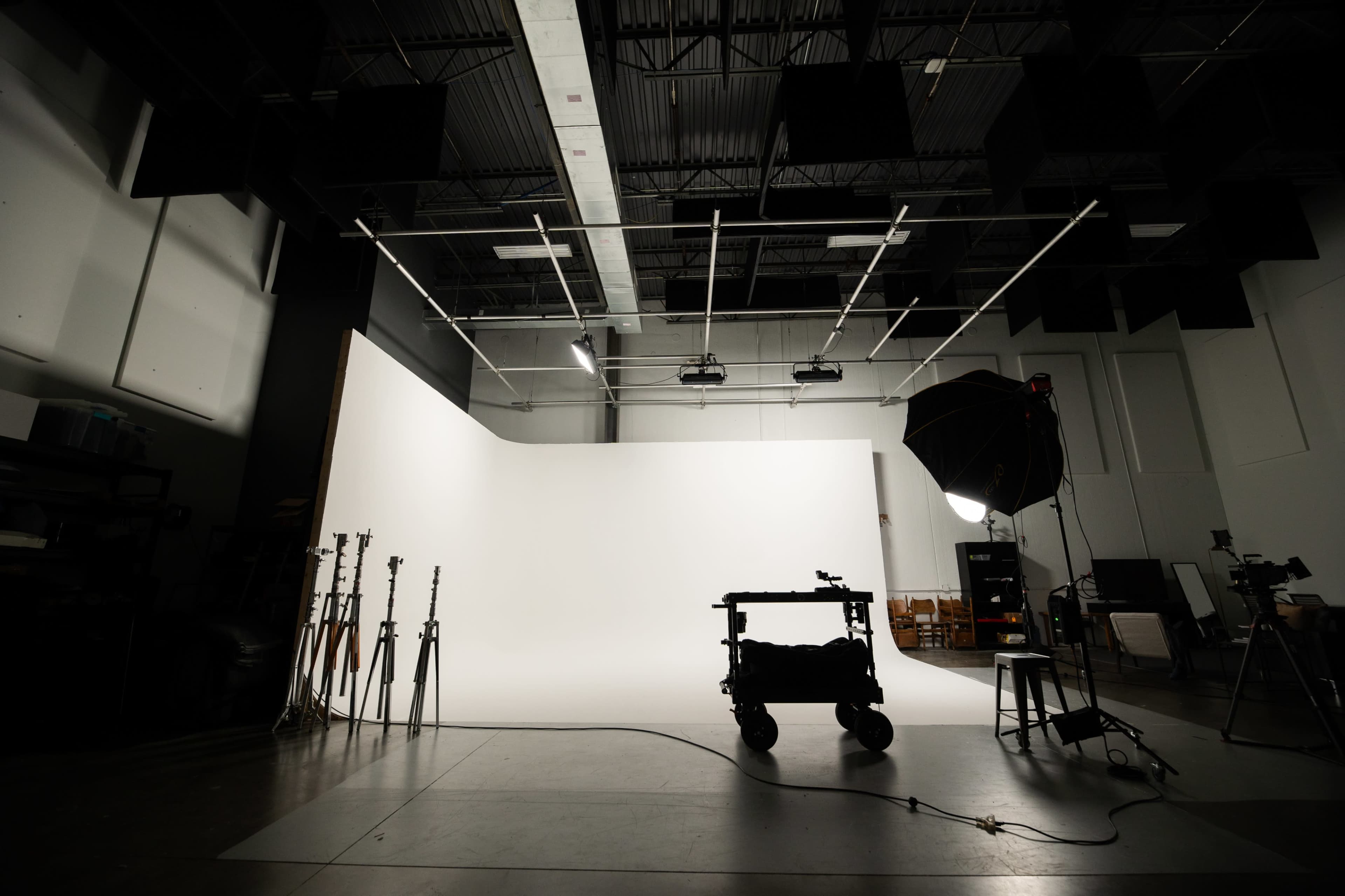 A photography studio features a large white backdrop, various lighting equipment, and a cart with tools set against a dark floor.