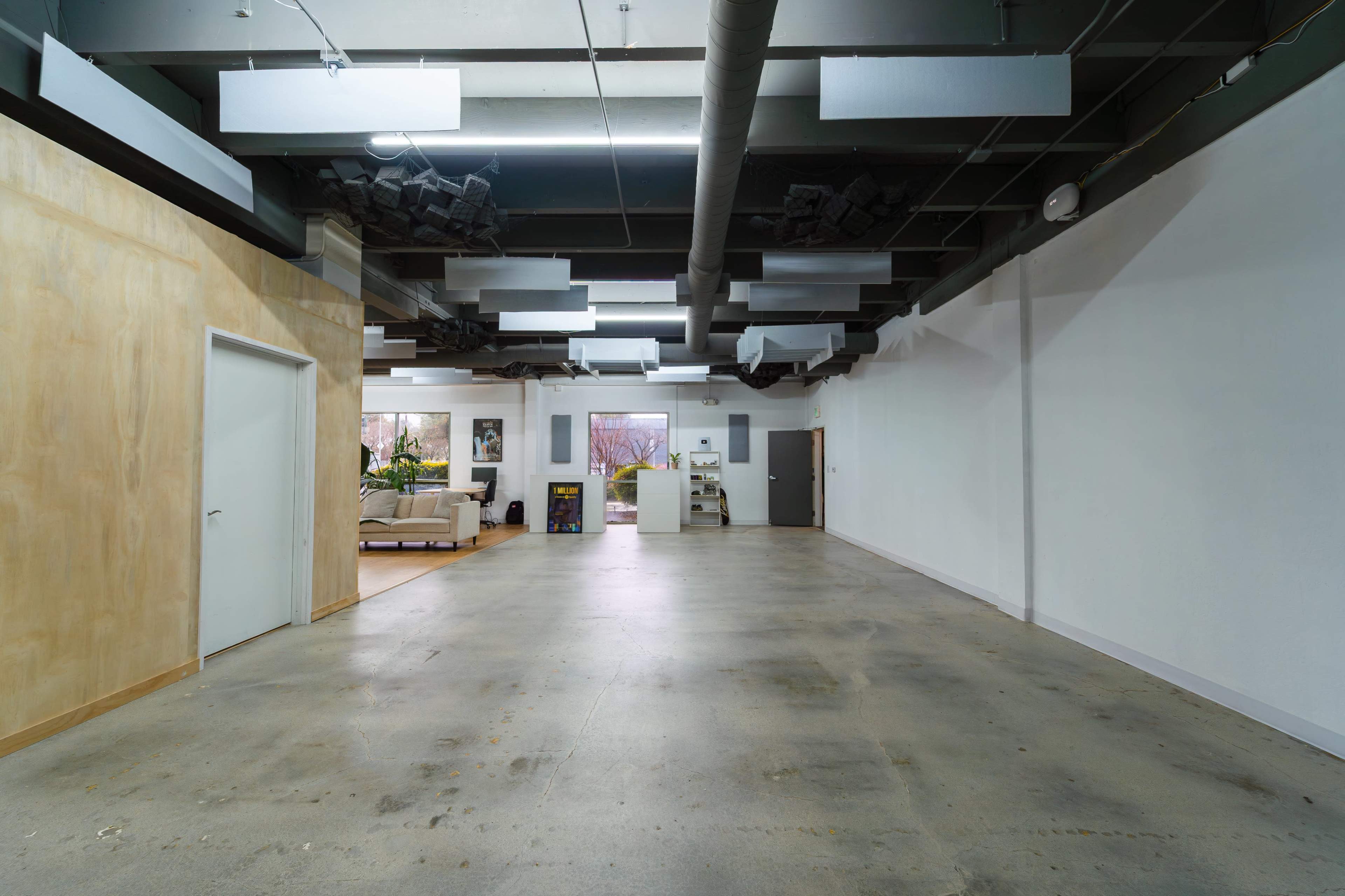 The image shows a spacious, empty interior room with a smooth concrete floor and a ceiling featuring exposed ductwork and sound-absorbing panels.