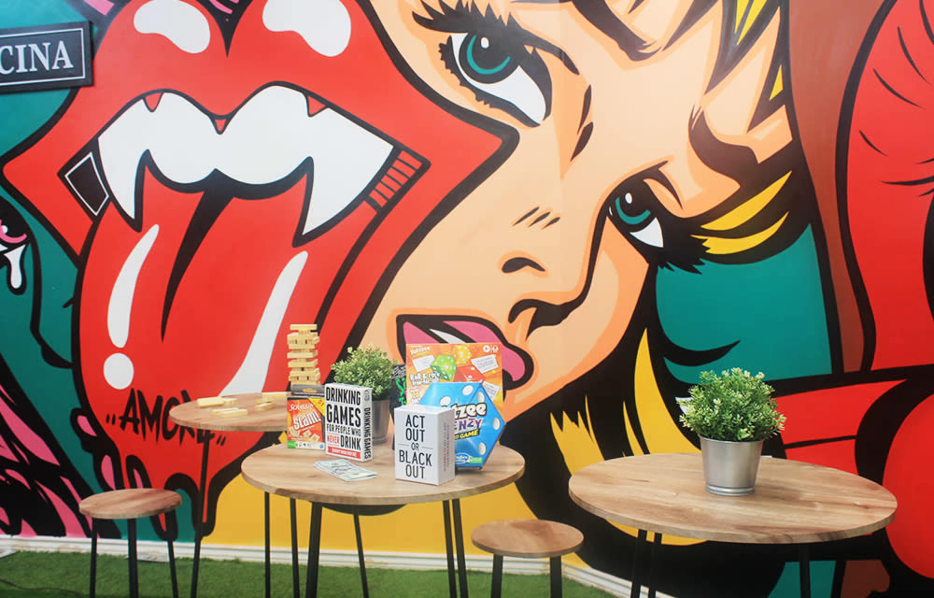 A vibrant mural of a woman's face alongside two round wooden tables with board games and small potted plants on them.