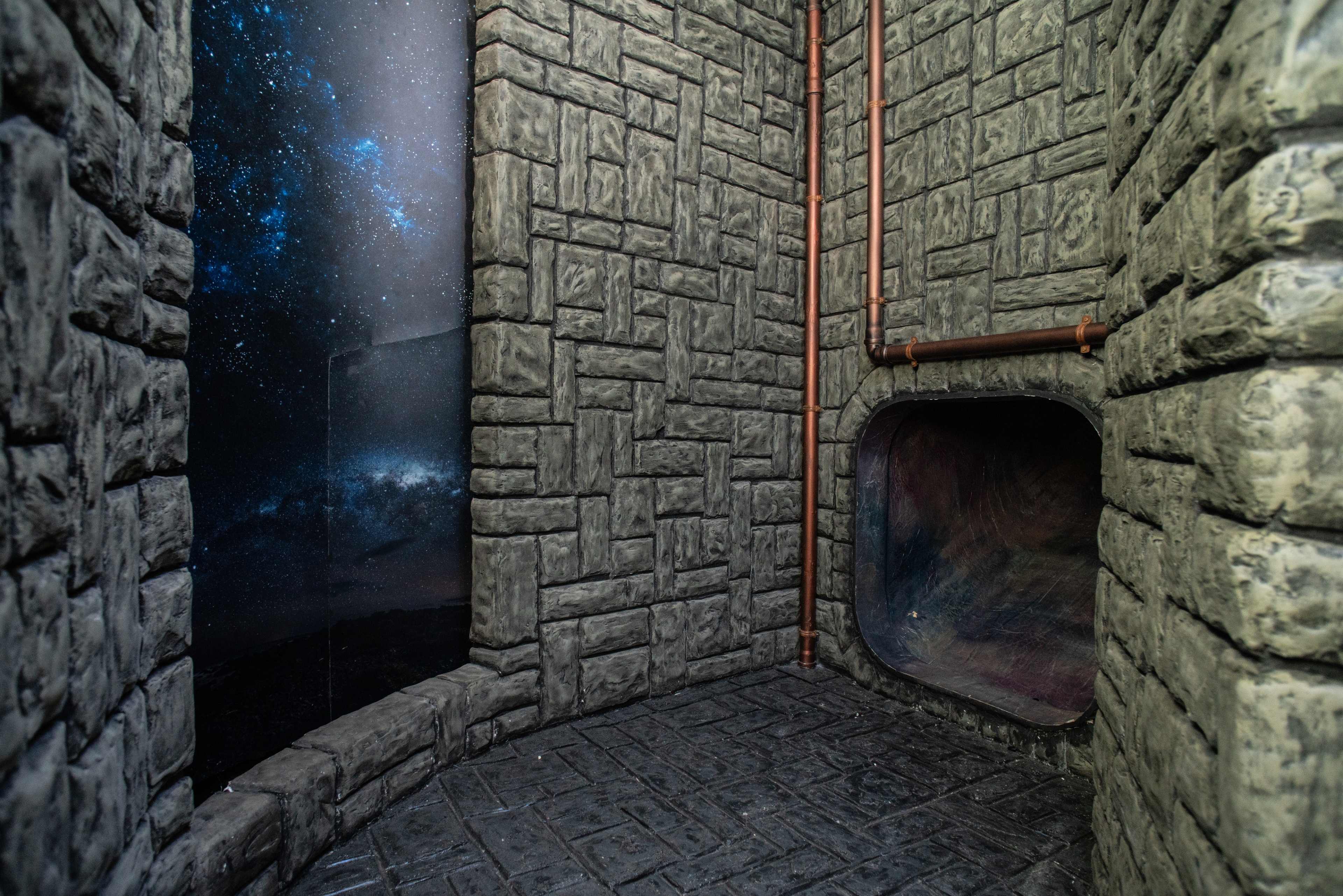 A corner of a room with stone-textured walls, a curved opening on one side, and a starry night sky mural on the opposite wall.