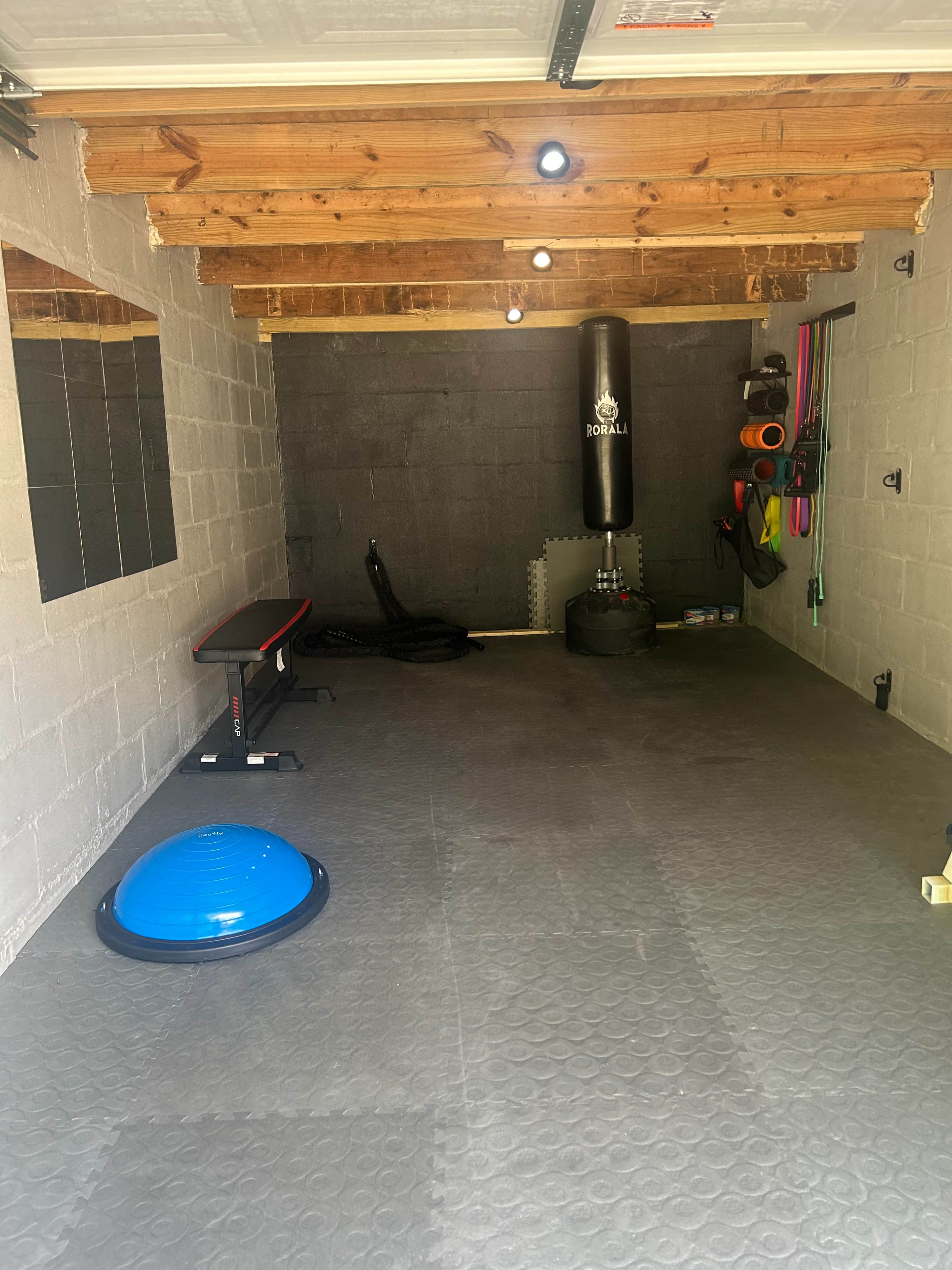 A well-organized home gym with fitness equipment including a bench, a punching bag, resistance bands, and a stability ball on a rubber floor.