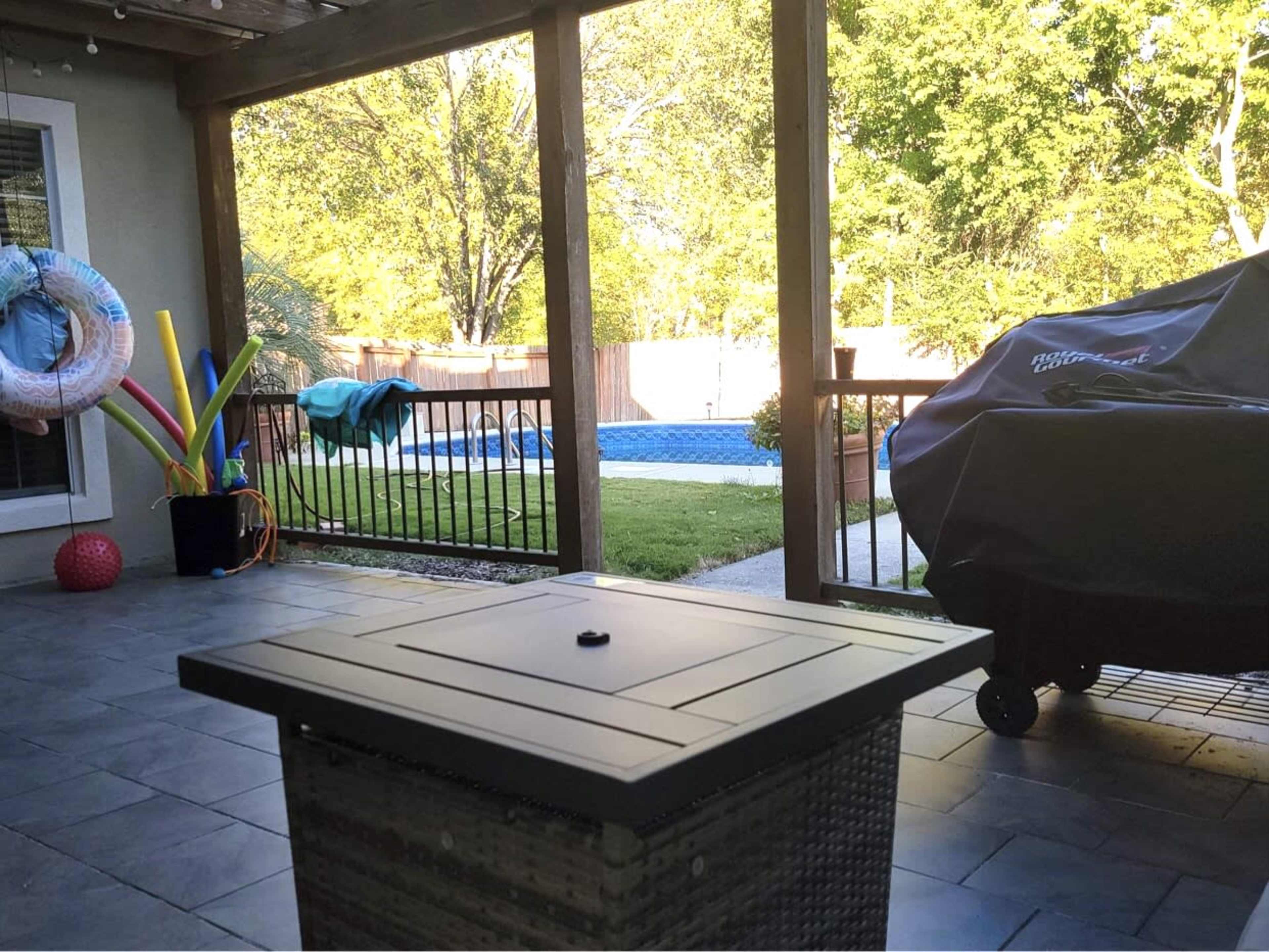 A patio area with a table at the forefront, viewing a backyard with a swimming pool and colorful pool toys nearby.