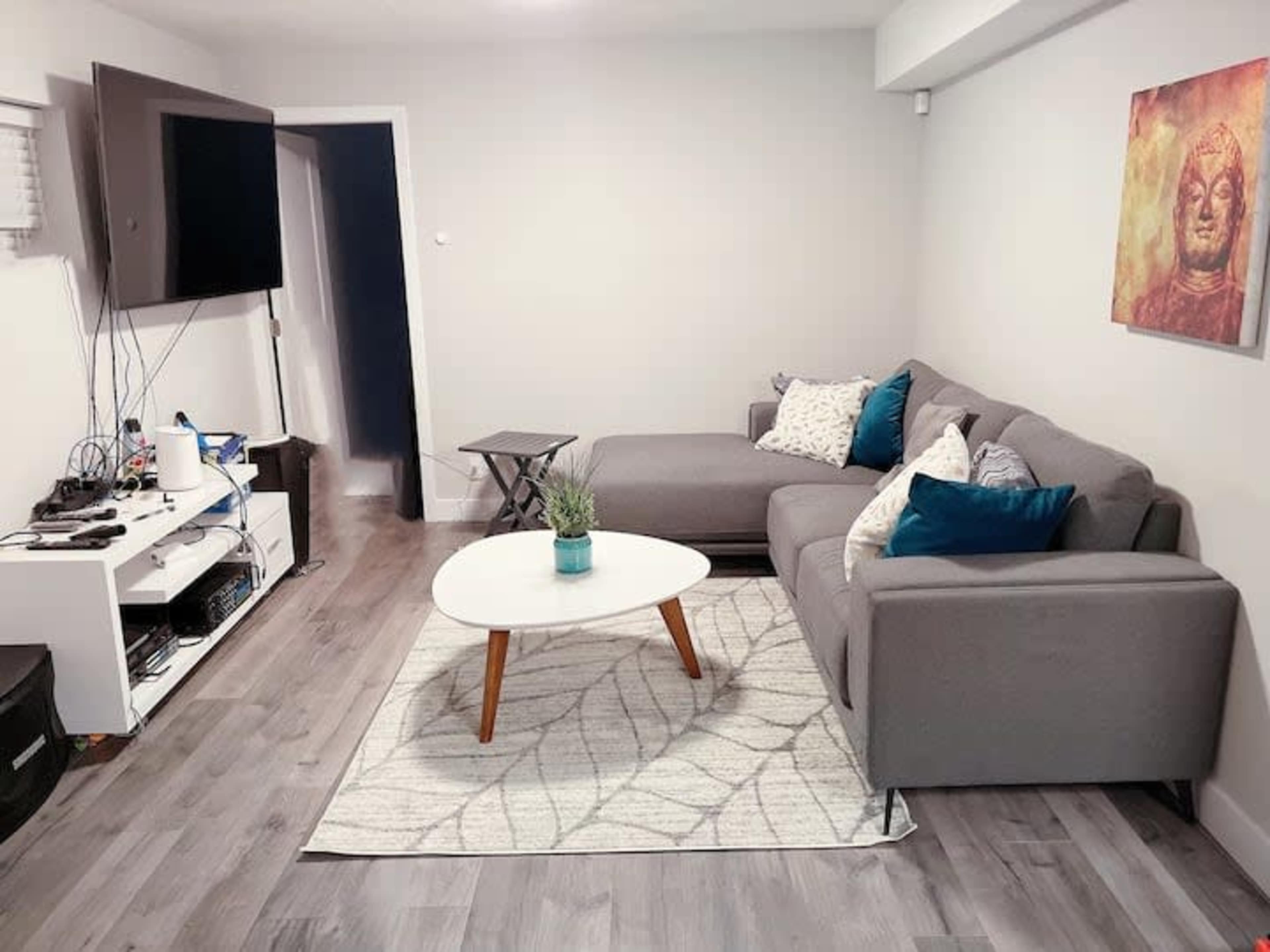 The image shows a living room with a gray couch, a white coffee table on a geometric rug, and a wall-mounted television.