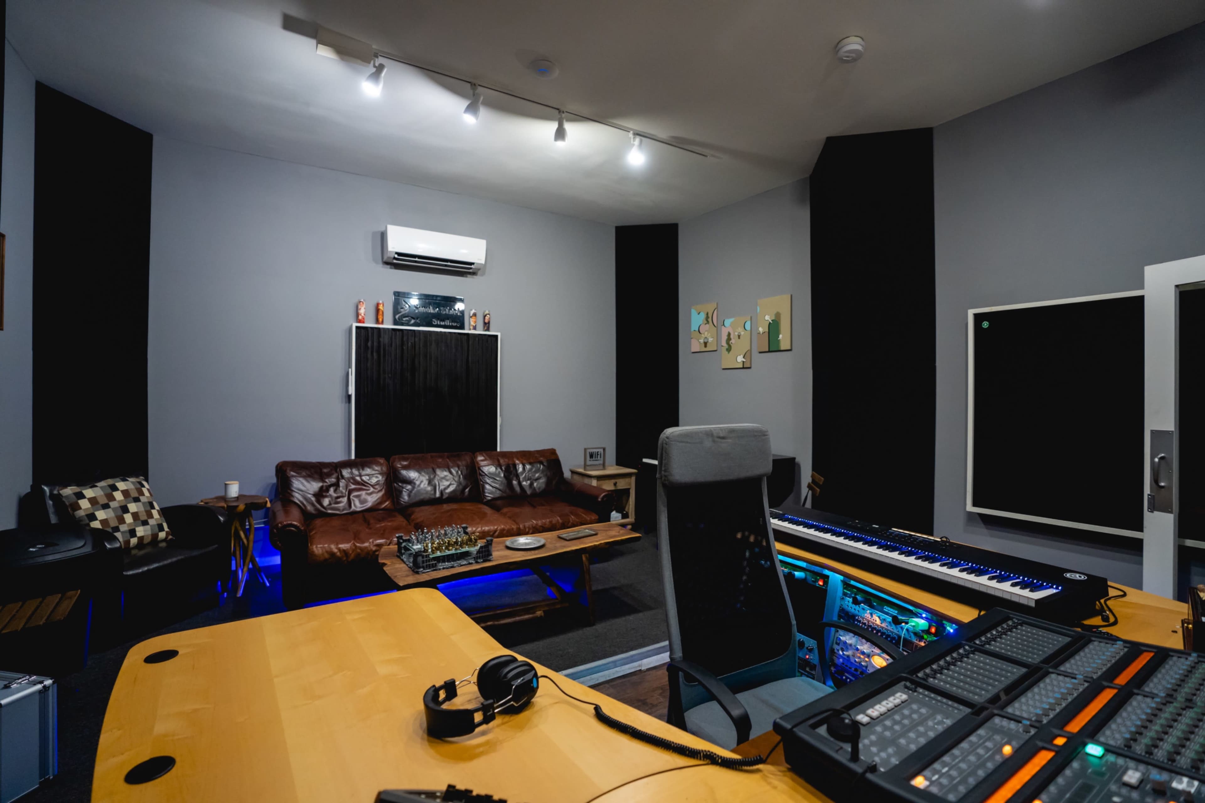 The image shows a music studio with a mixing desk, a leather sofa, and soundproofing panels on the walls.