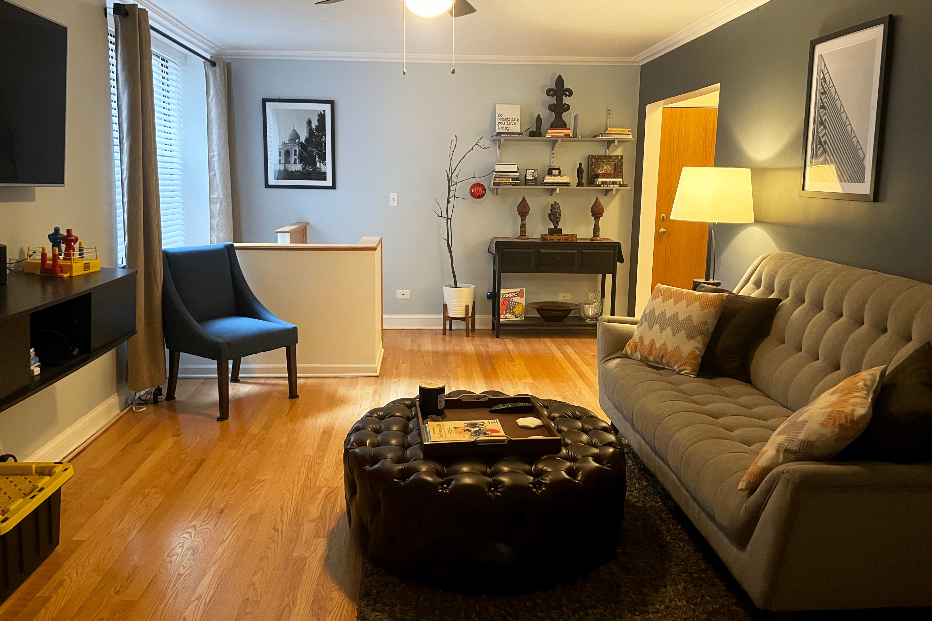 A living room with a gray couch, a round ottoman, a blue accent chair, and a wall-mounted television.