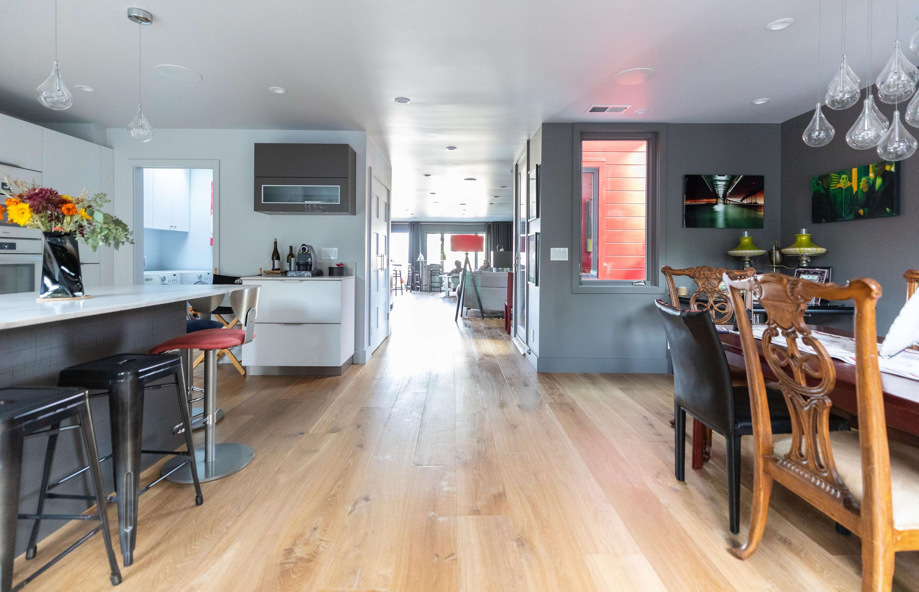 A modern open-plan kitchen and dining area with wooden flooring, natural light, and a mix of furniture styles.