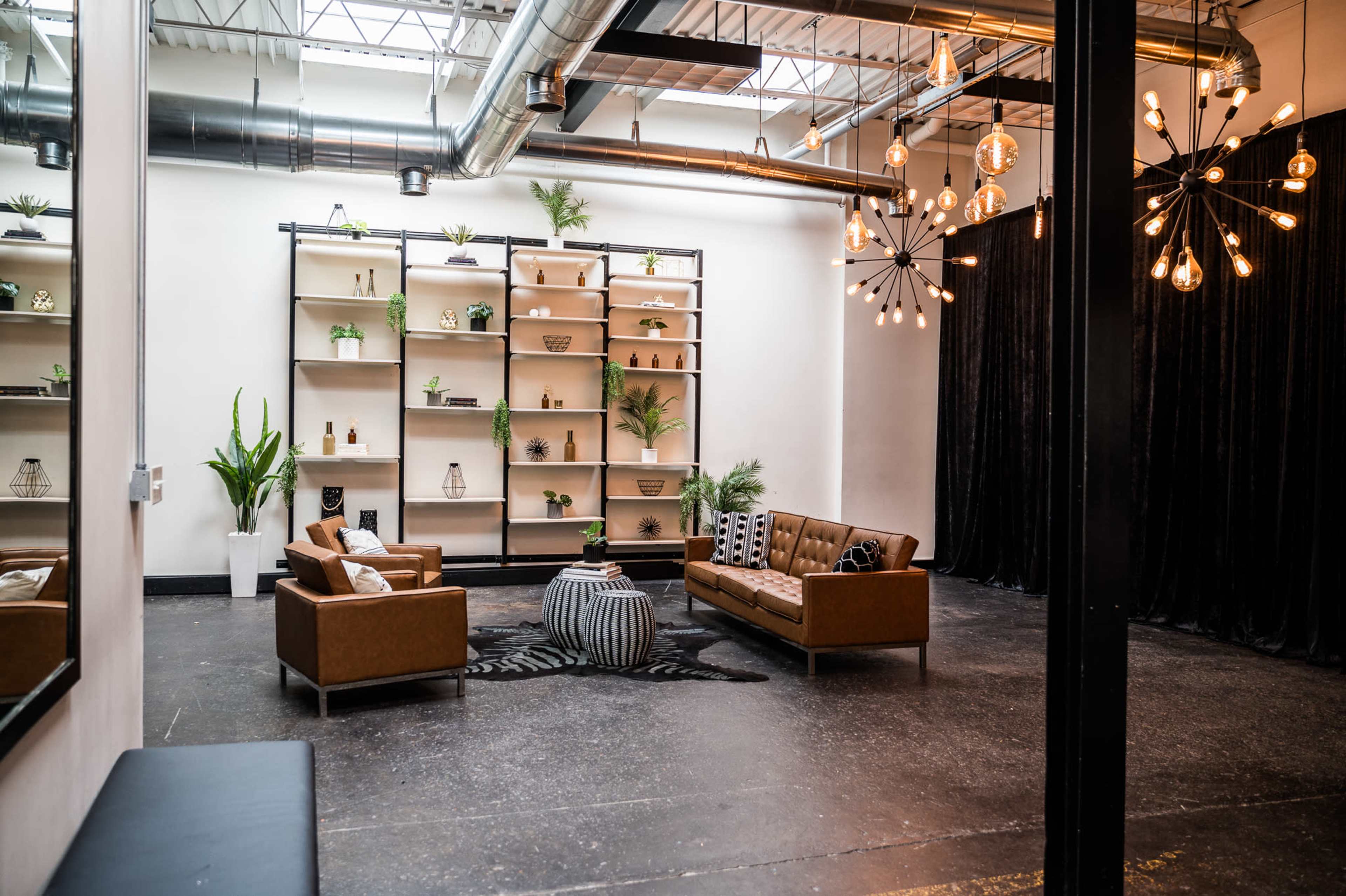 A modern lounge area featuring two brown sofas, a round coffee table, and a shelving unit with decorative plants and objects against a black draped wall.