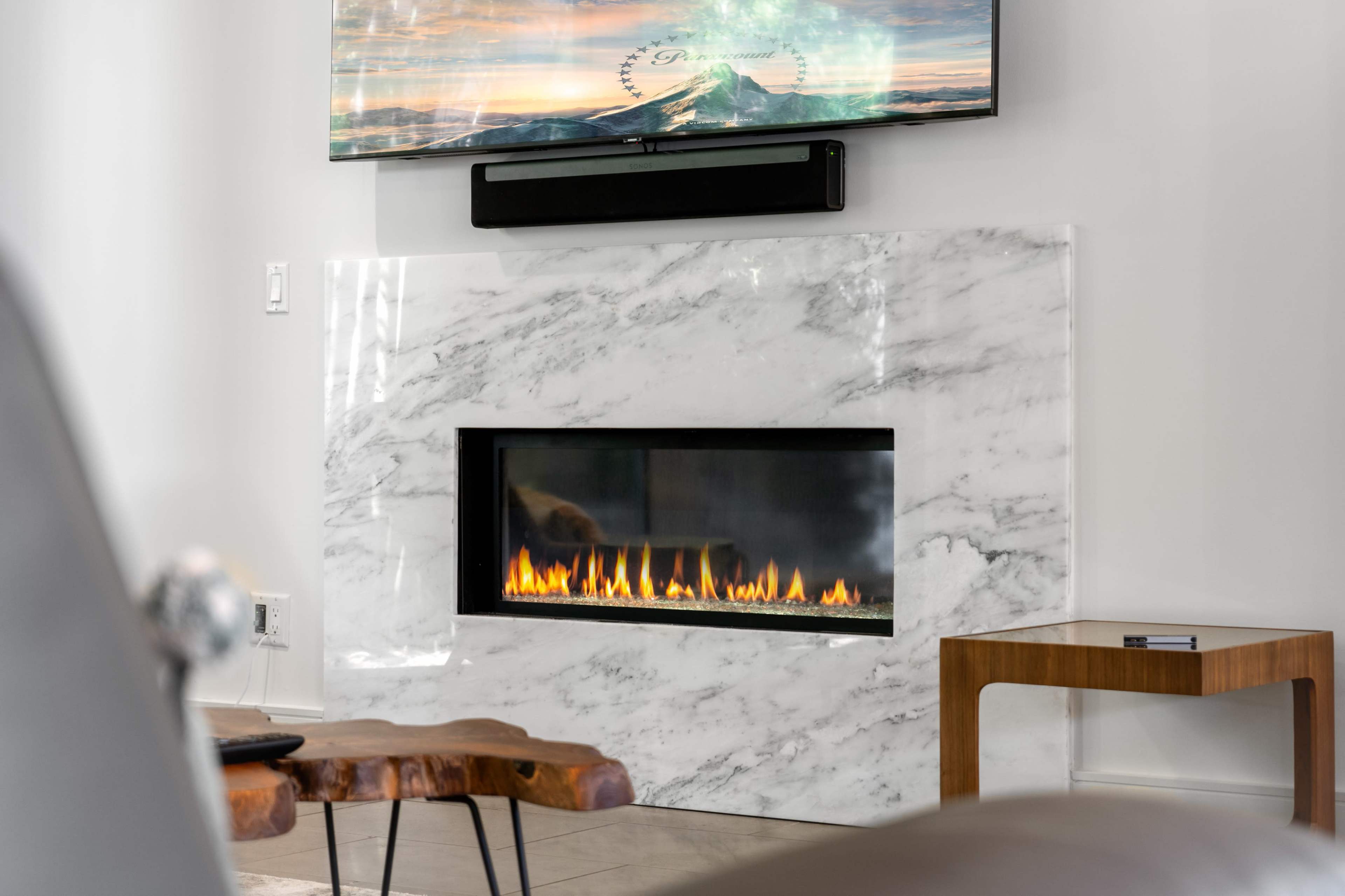 A modern living room featuring a marble fireplace with a linear flame and a television mounted above it.