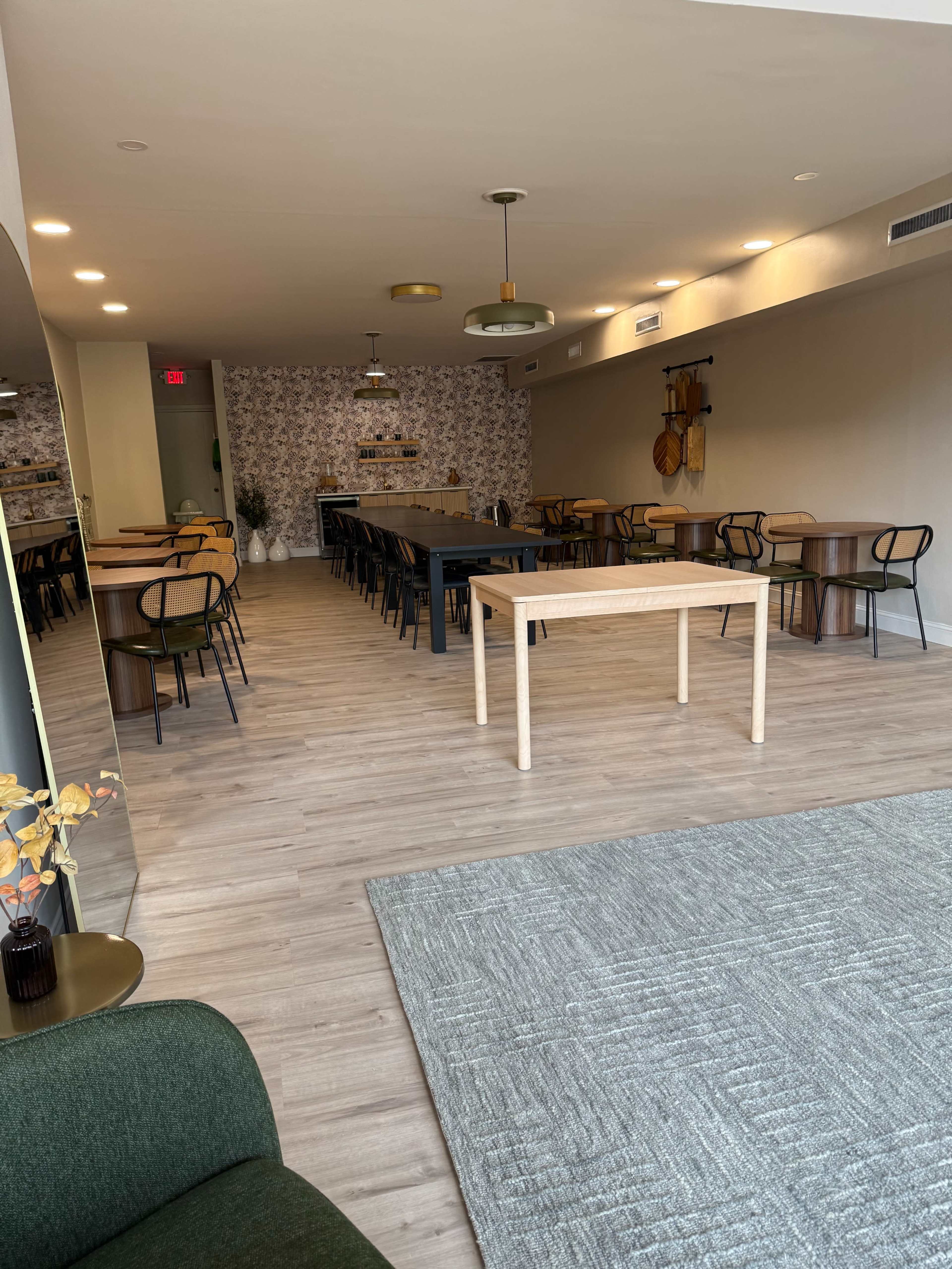The image shows a spacious, modern dining area with a long central table, wooden chairs, and decorative wallpaper.