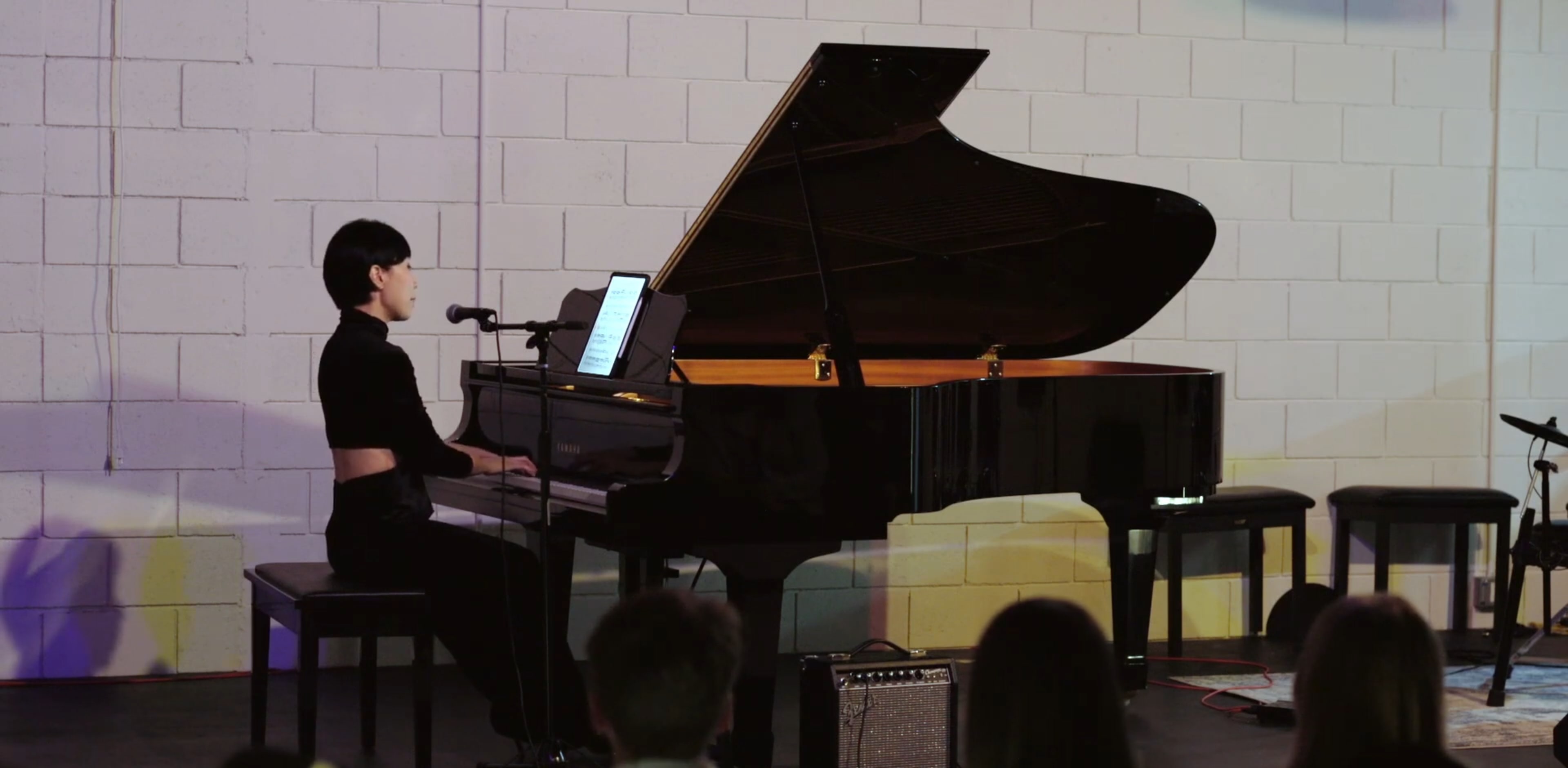 A musician plays a grand piano while singing into a microphone in a staged performance setting.