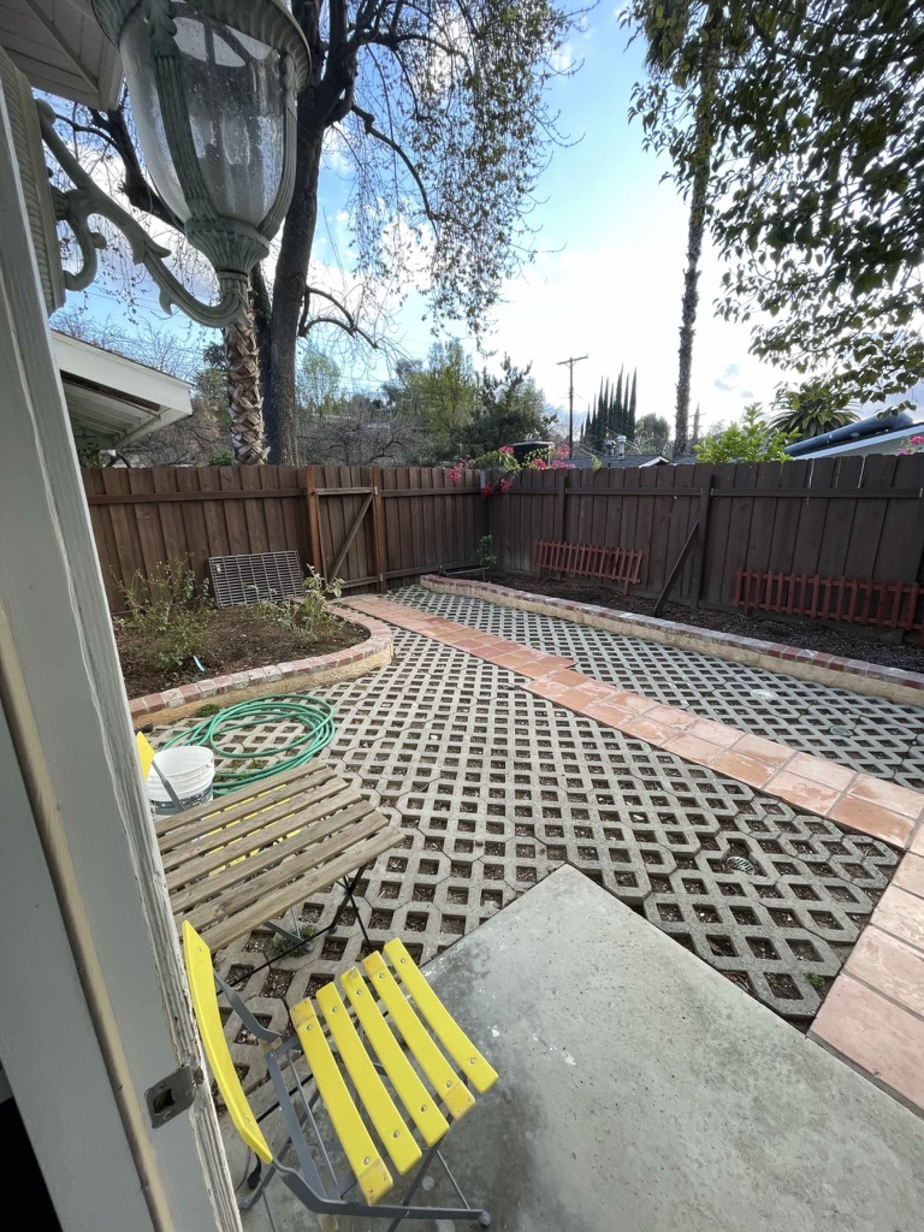 A garden area features a gravel and tile pathway surrounded by a wooden fence, benches, and a few plants.