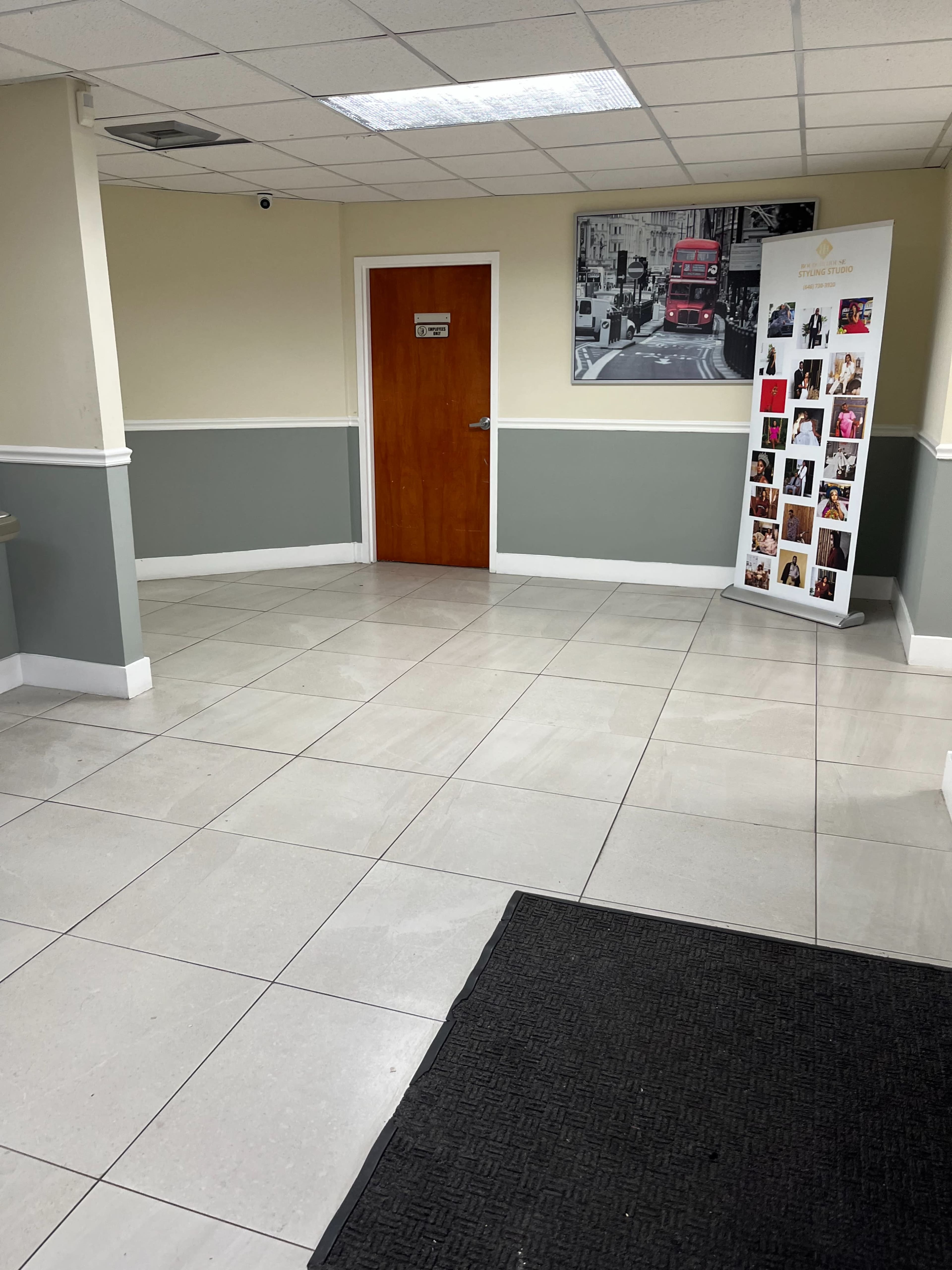 A well-lit reception area features gray and white walls, a wooden door, and a banner displaying photographs.