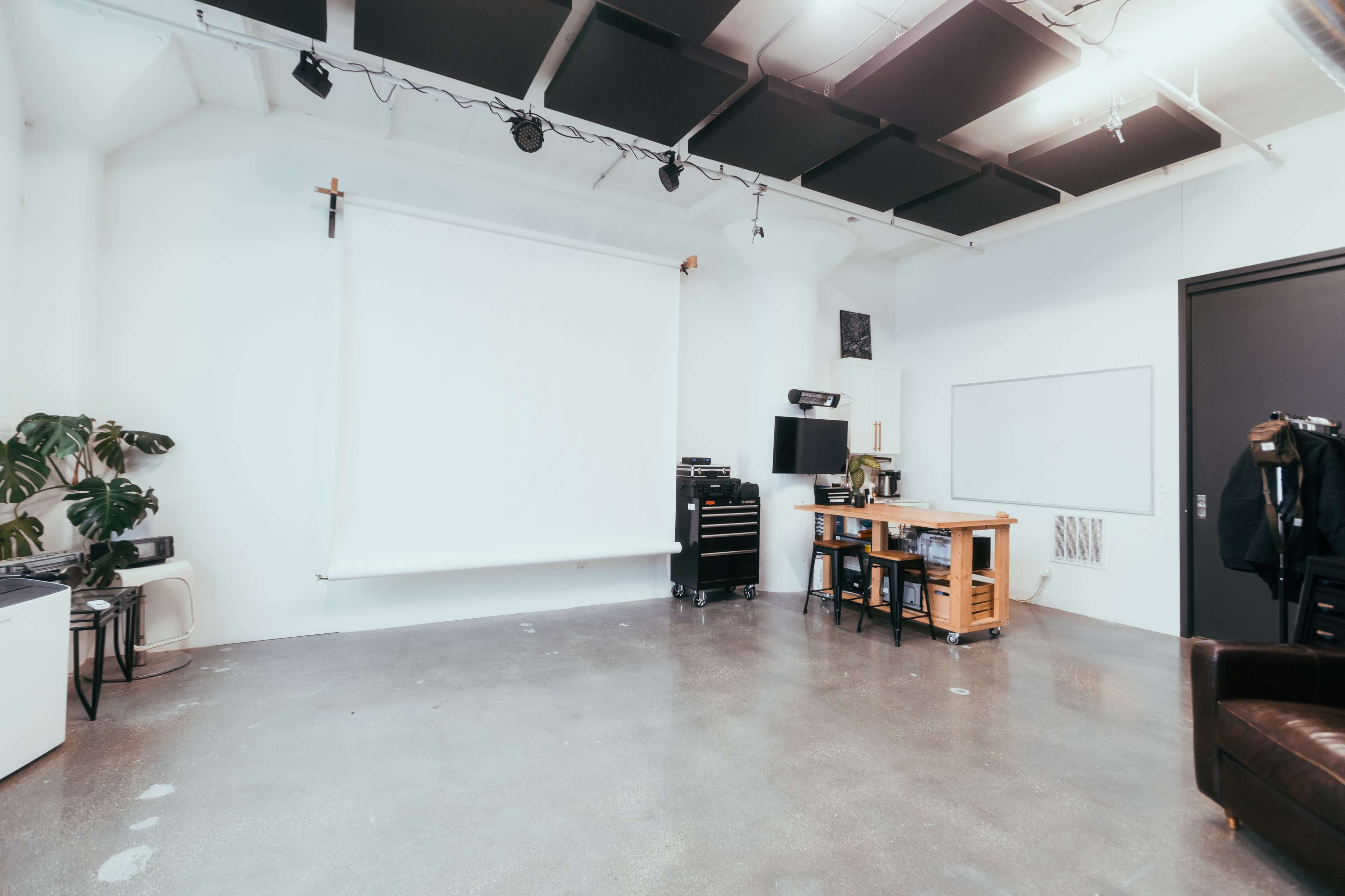 The image shows a spacious, well-lit studio with a blank backdrop, a work table, and various furniture and equipment.