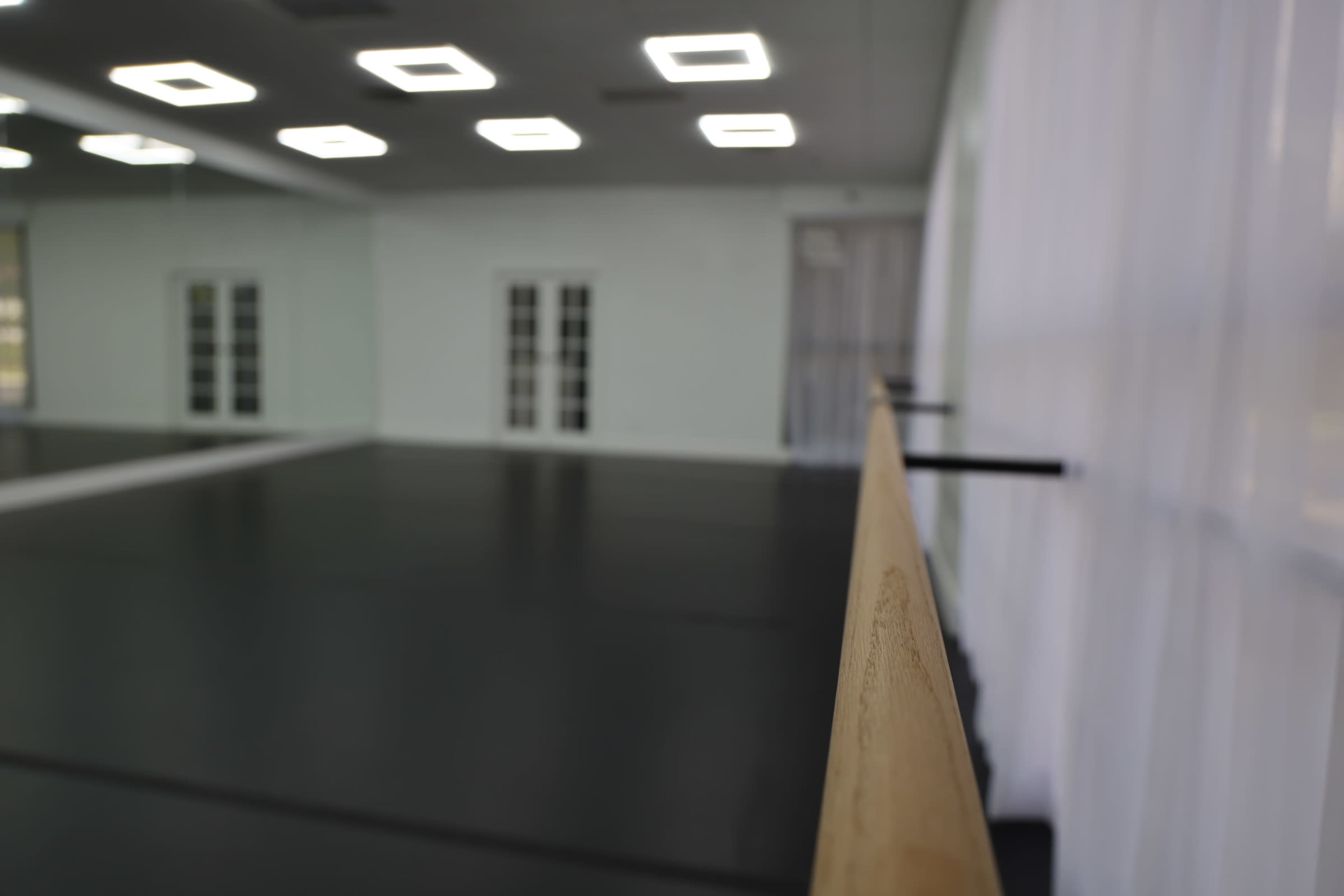 The image shows a dance studio with a wooden barre along one wall, large mirrors, and soft overhead lighting.