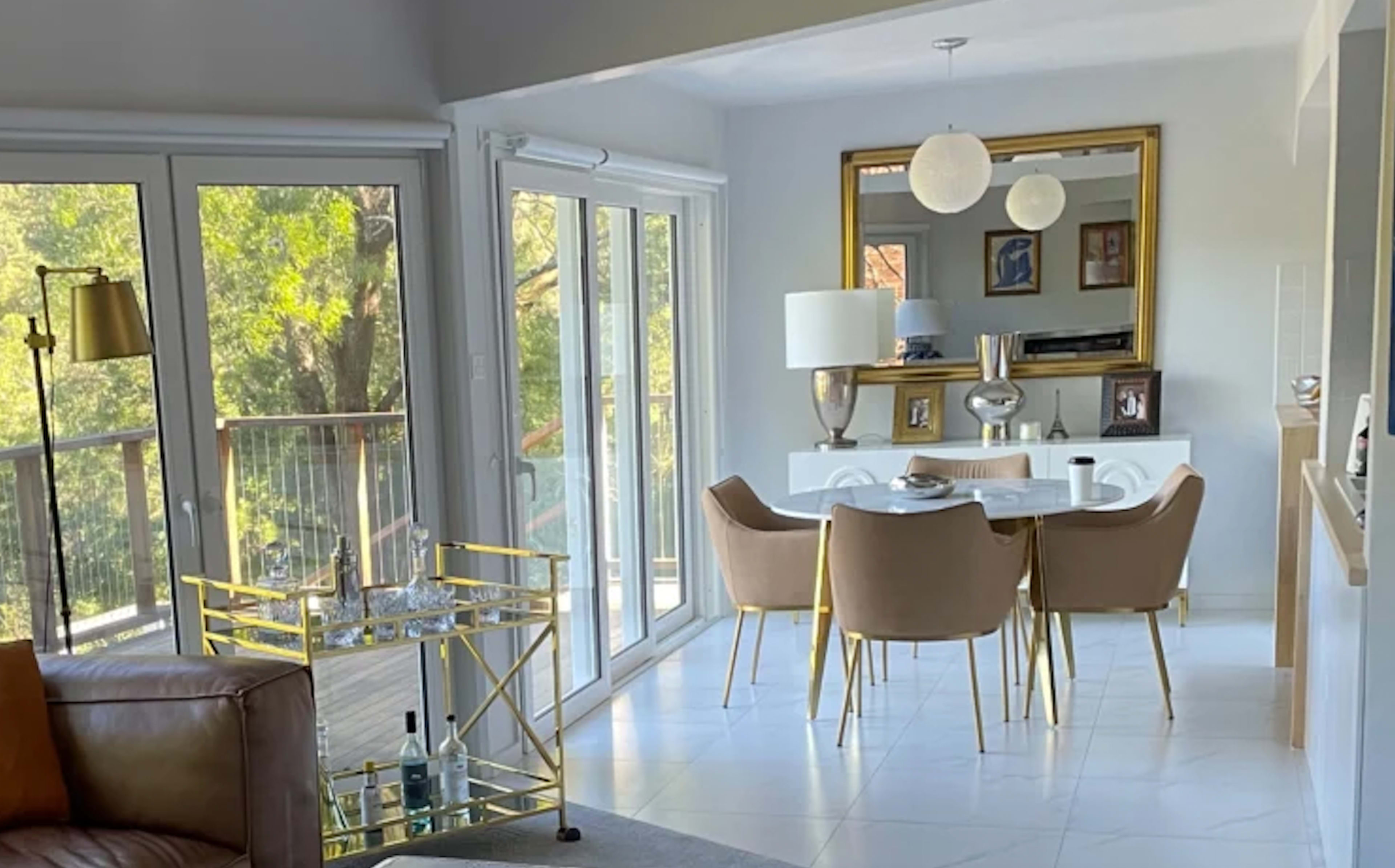 A dining area features a table surrounded by chairs, a large mirror on the wall, and large windows letting in natural light.