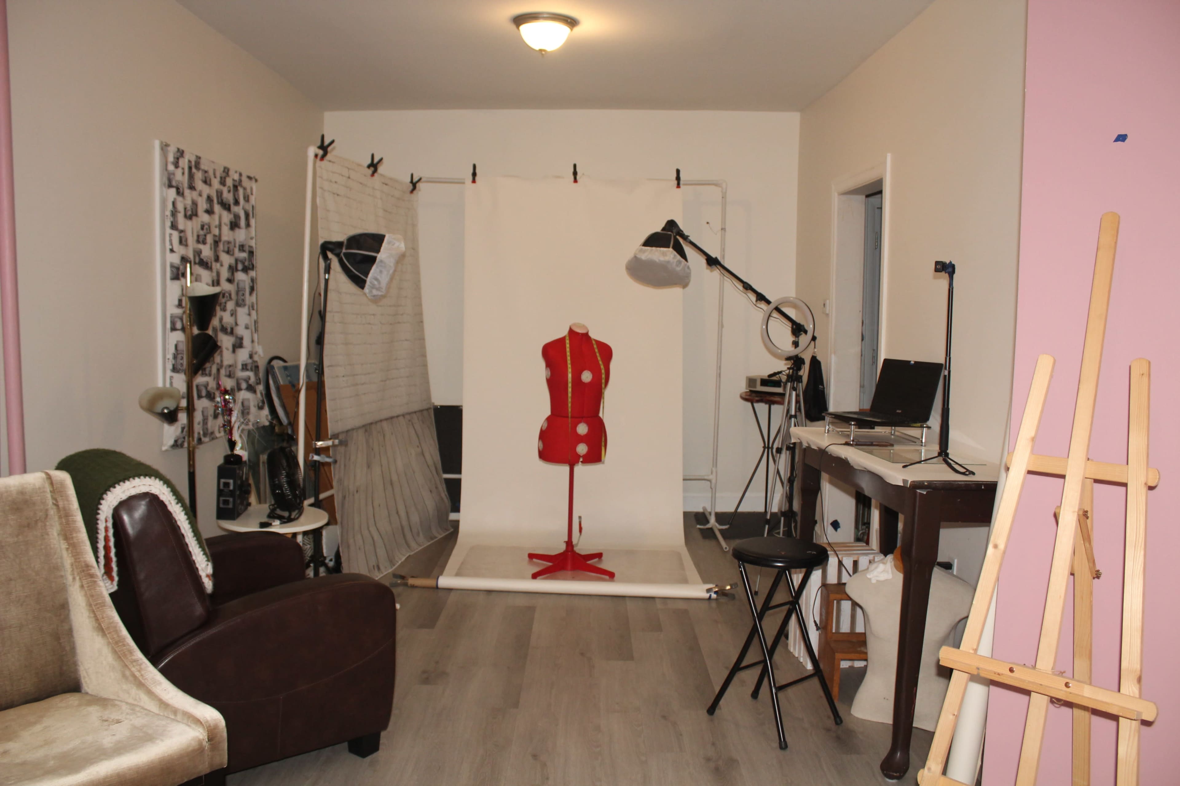 The image shows a styled interior space with a sewing mannequin at the center, surrounded by various tools and furniture used for crafting or design work.