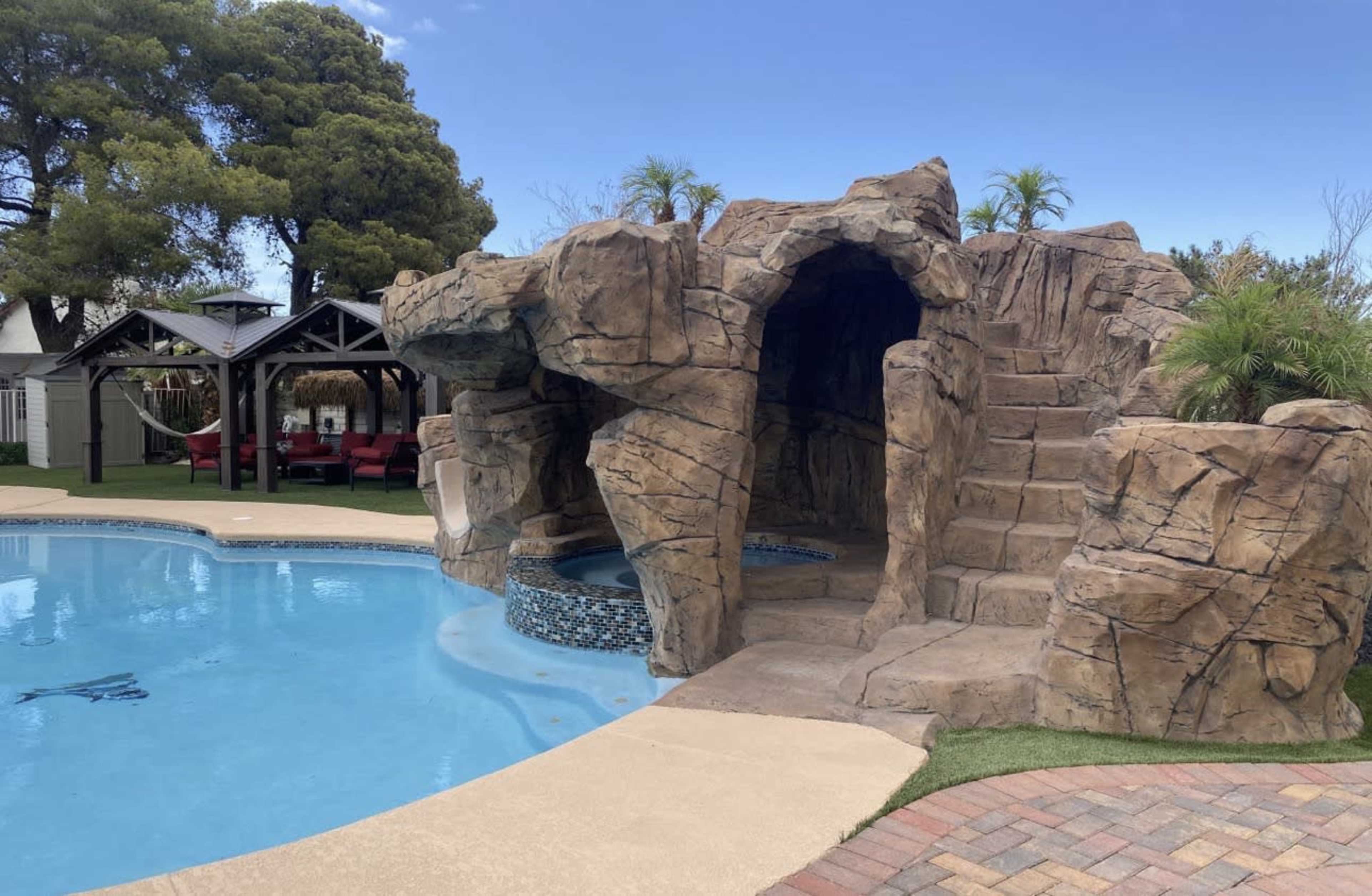 A swimming pool features a rock formation that includes a cave entrance and a staircase leading to a raised platform.