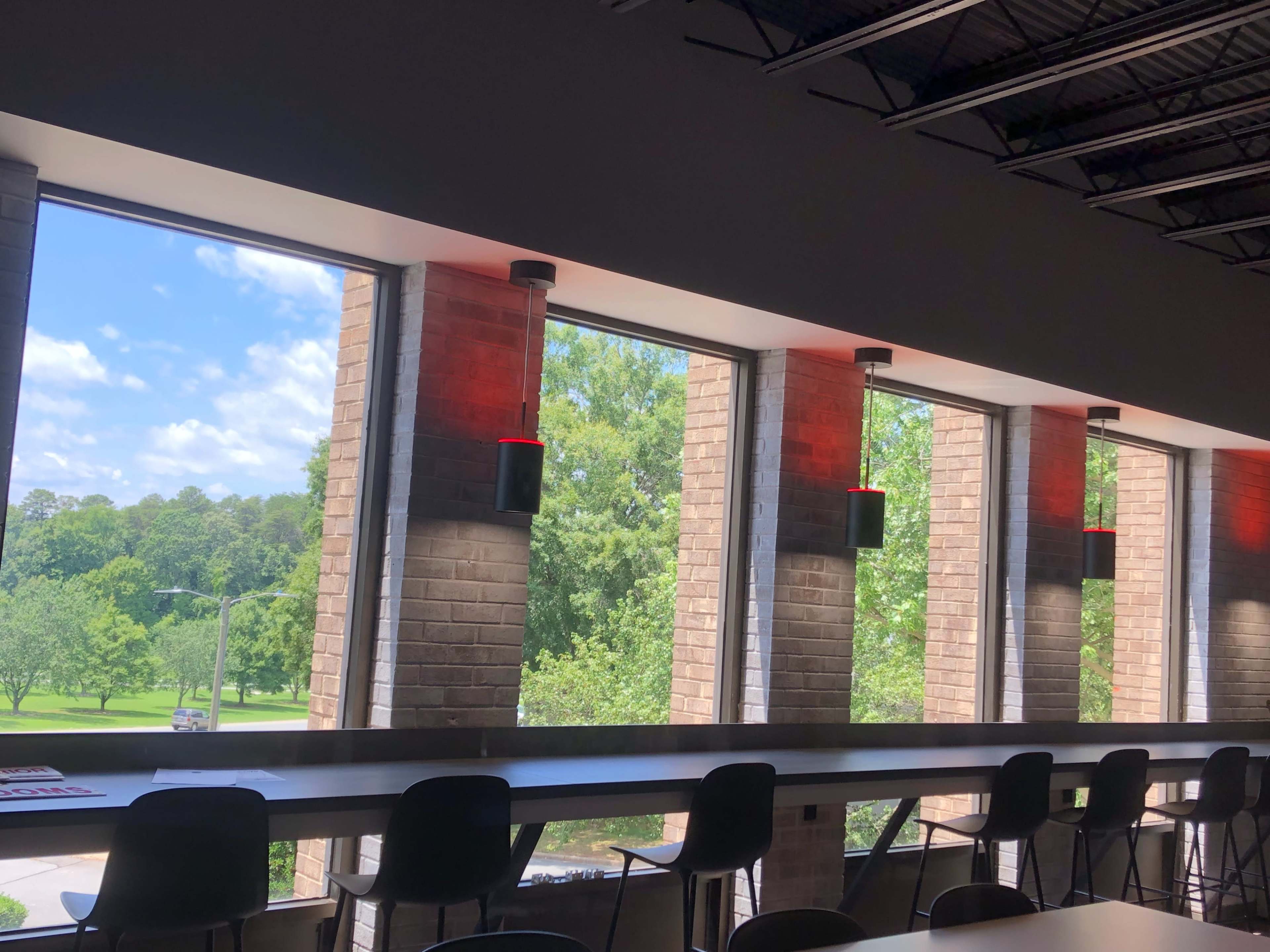 A modern interior with large windows and a row of black chairs along a concrete counter, illuminated by red lights on the walls.