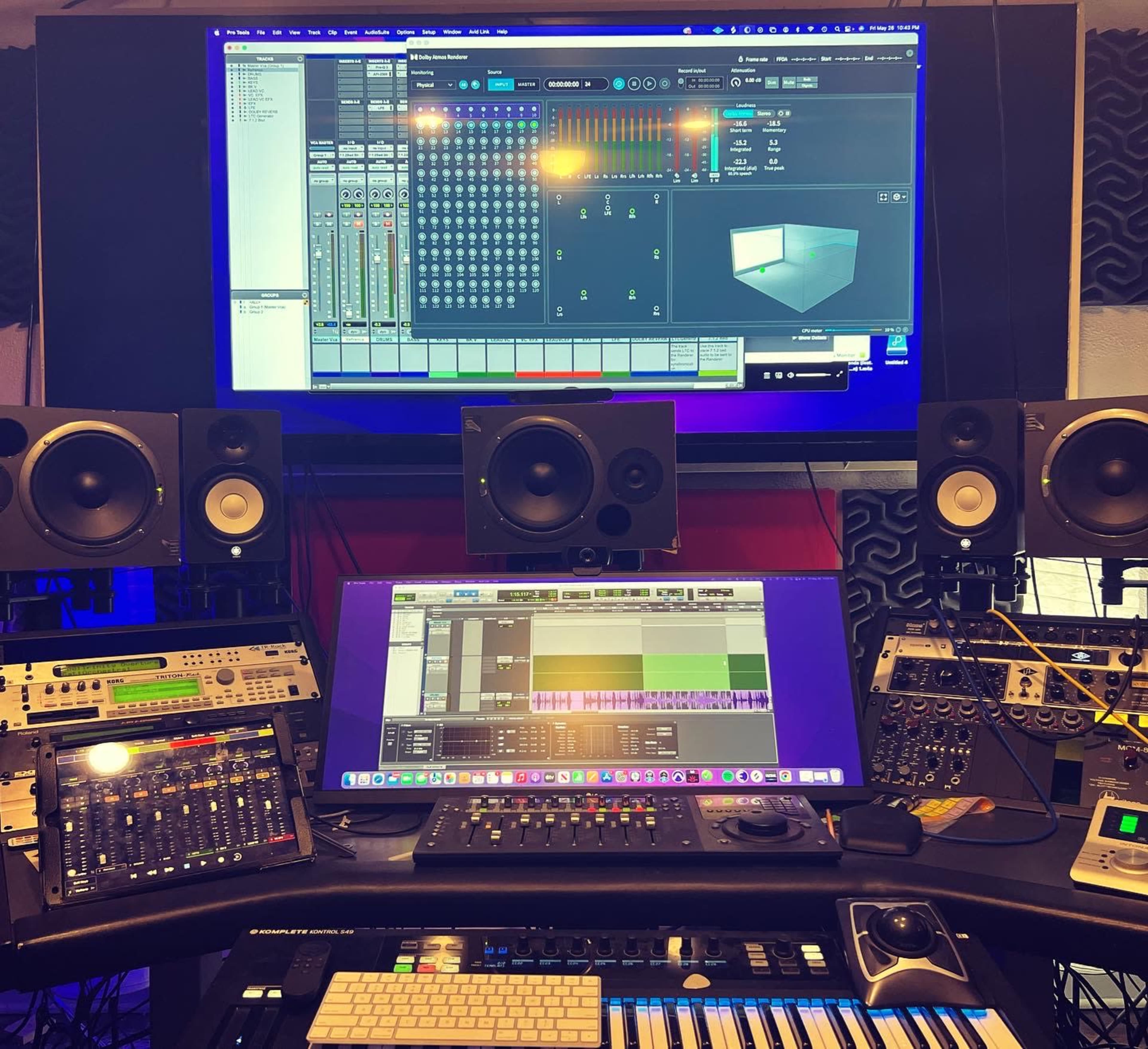 A music production studio with multiple audio speakers, a control surface, a keyboard, and a computer monitor displaying audio mixing software.