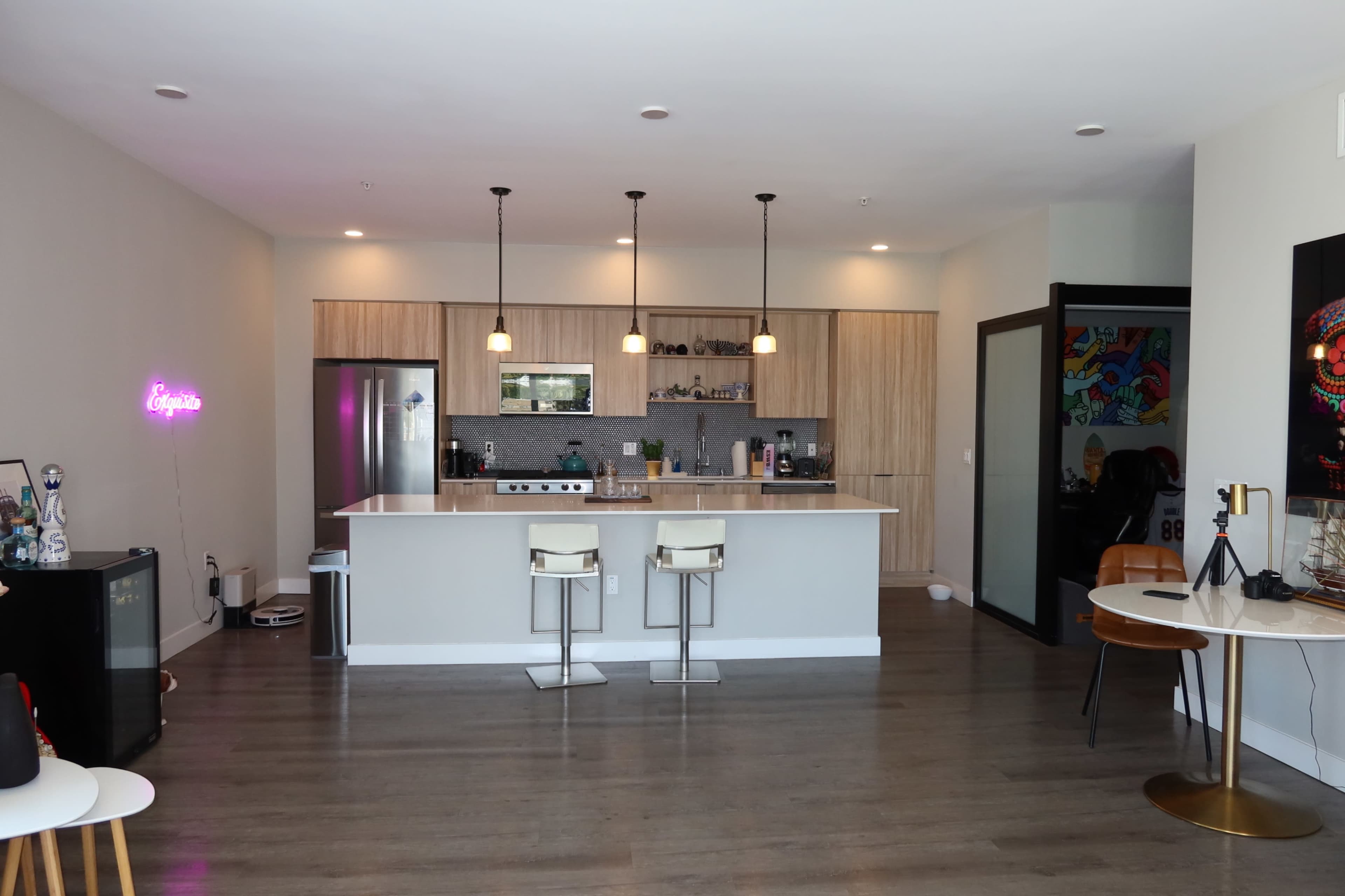 The image shows a modern kitchen with a central island, bar stools, and light wood cabinetry.