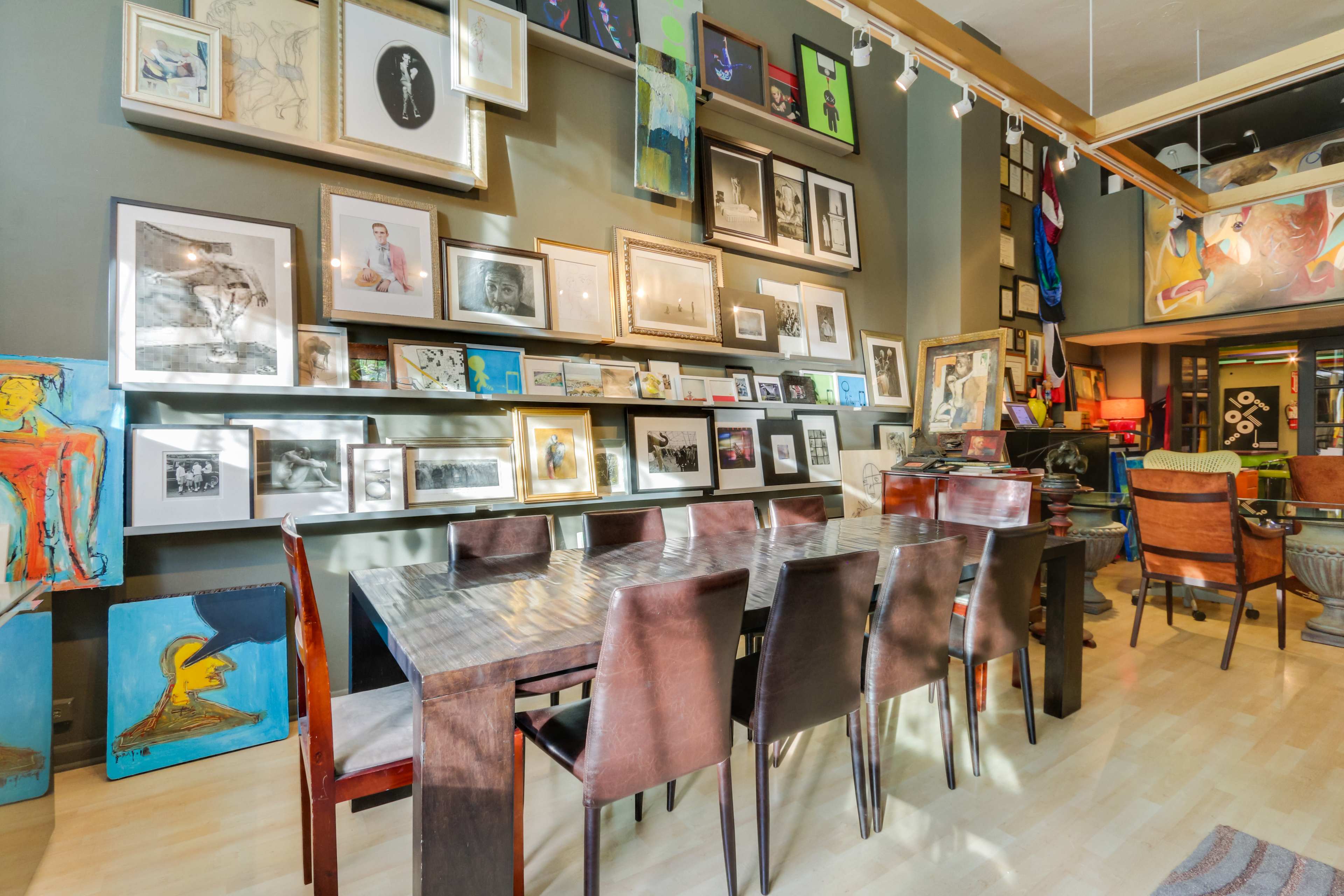 A gallery-style dining area with a long wooden table surrounded by chairs, adorned with an array of framed artworks on the walls.