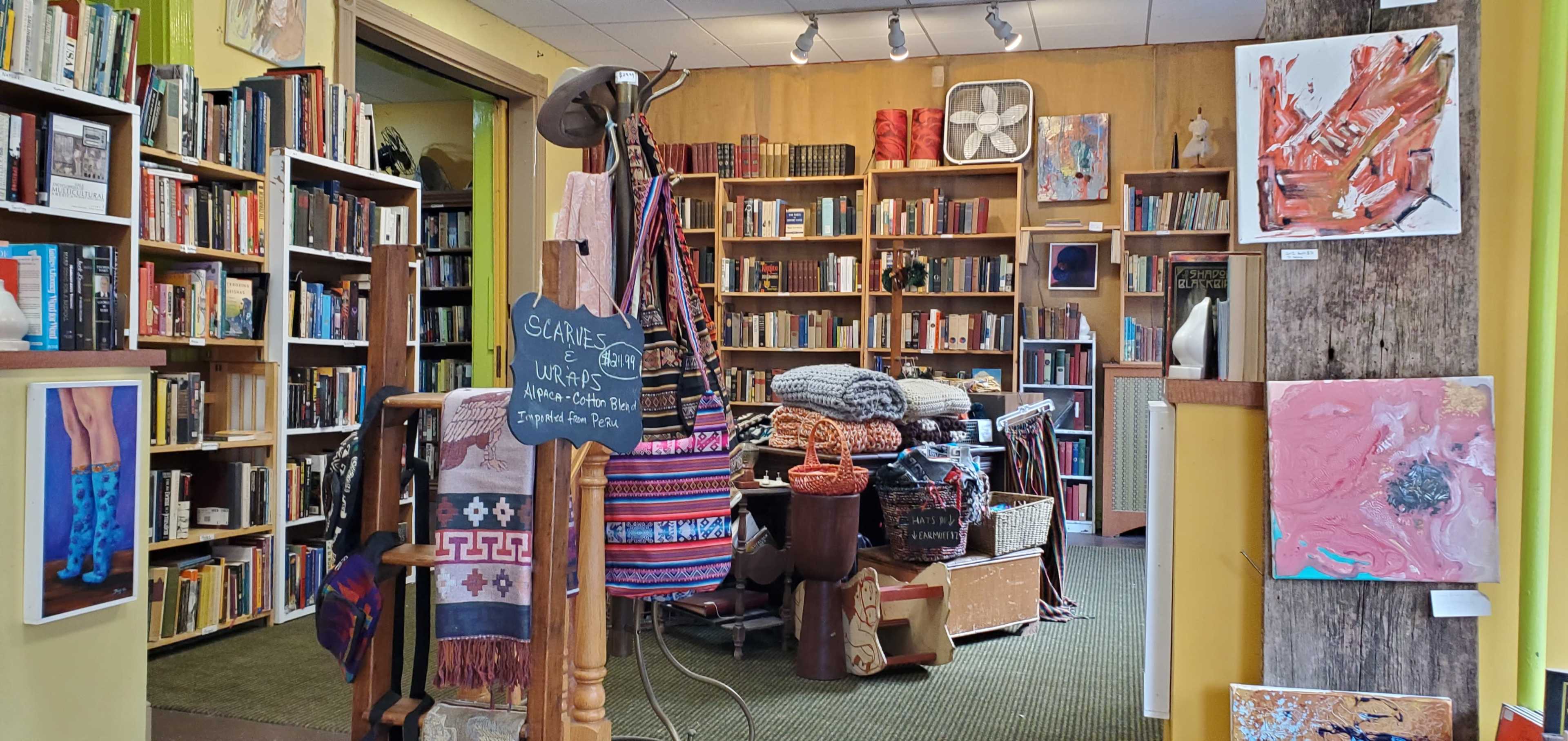A cozy interior of a bookstore featuring shelves filled with books, a display of handmade goods, and colorful artwork on the walls.