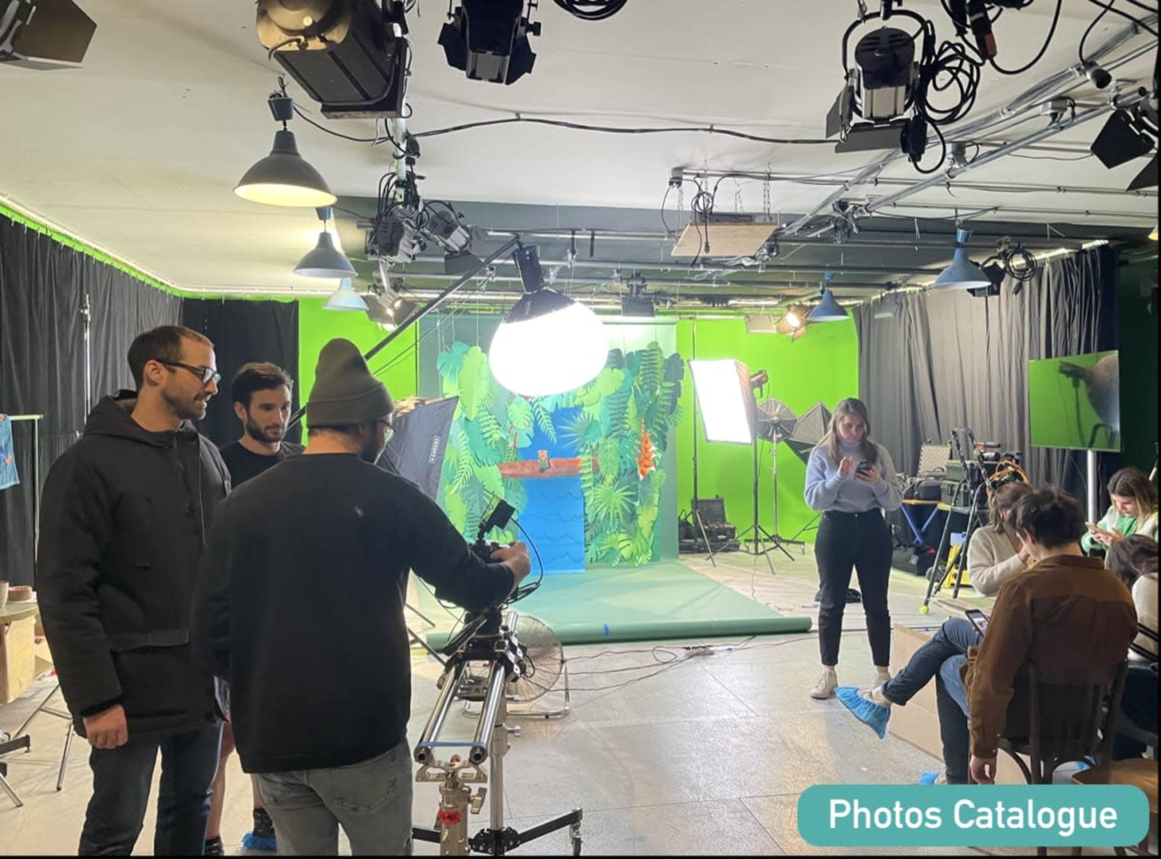 A group of people is preparing equipment in a film studio with a green screen and various lighting setups.
