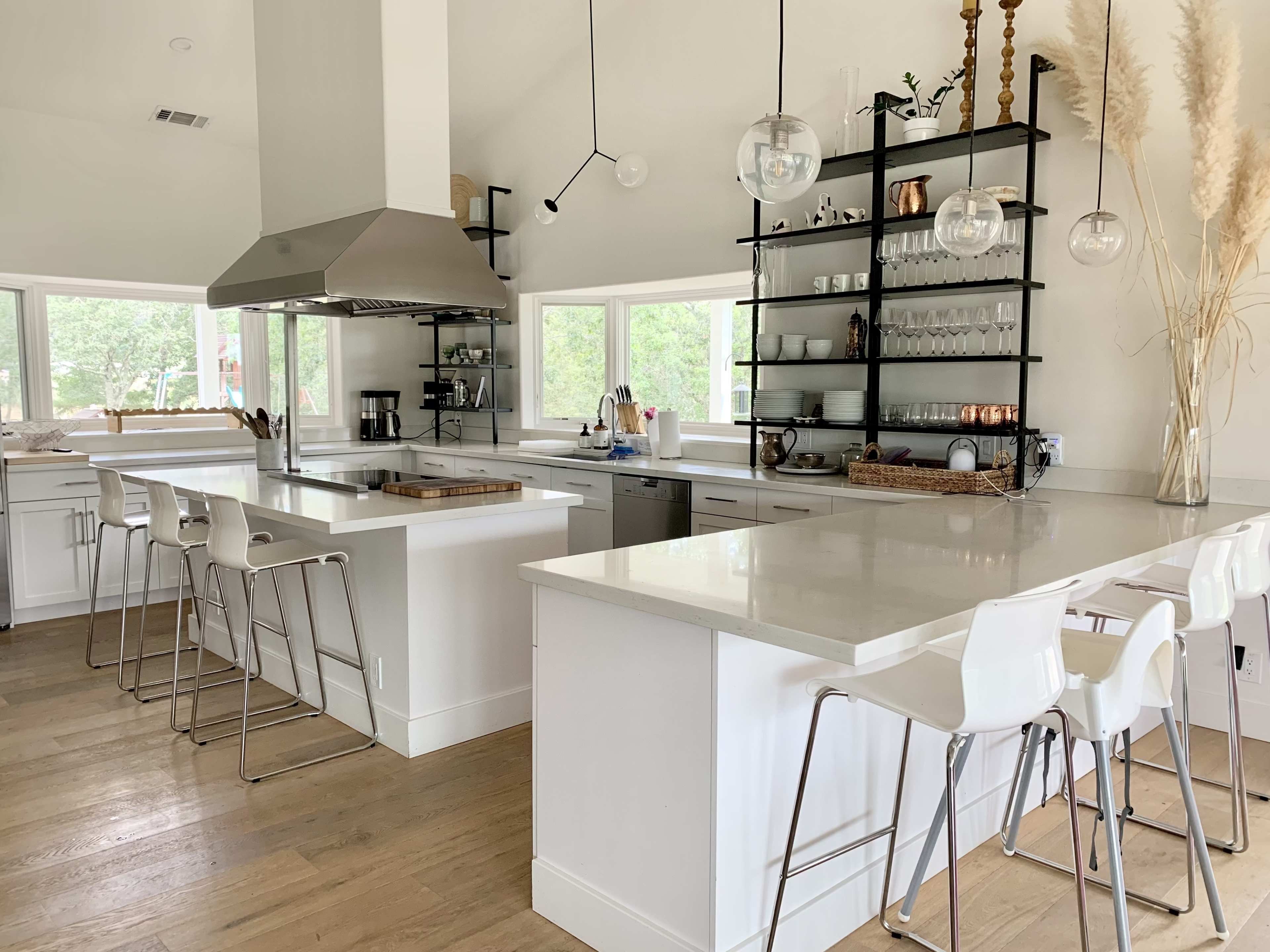A modern kitchen with white cabinetry, an island with bar stools, and large windows allowing natural light.