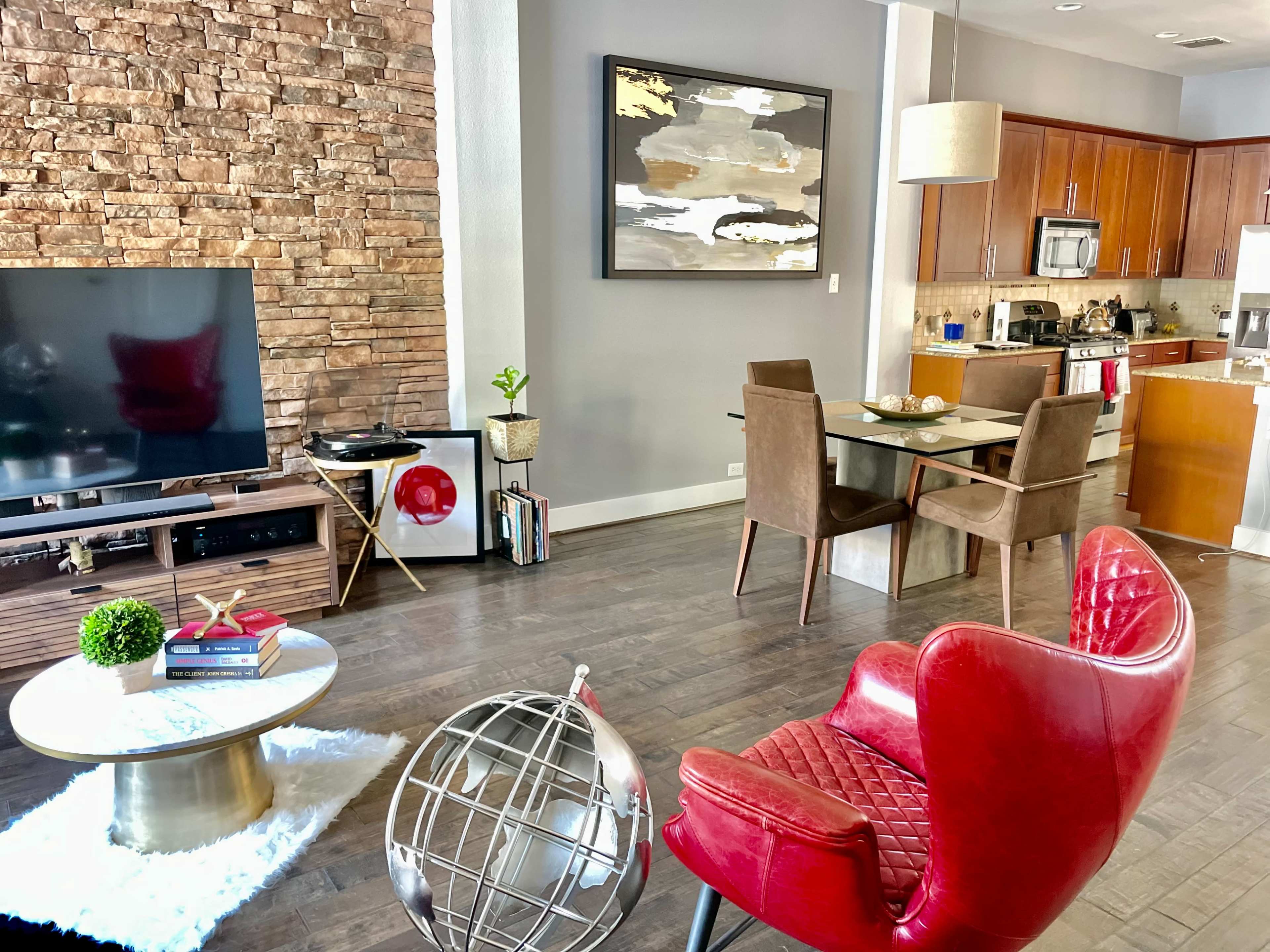 A modern living room with a stone accent wall, a television on a wooden stand, a dining area with a small table and chairs, and a decorative globe on a coffee table.