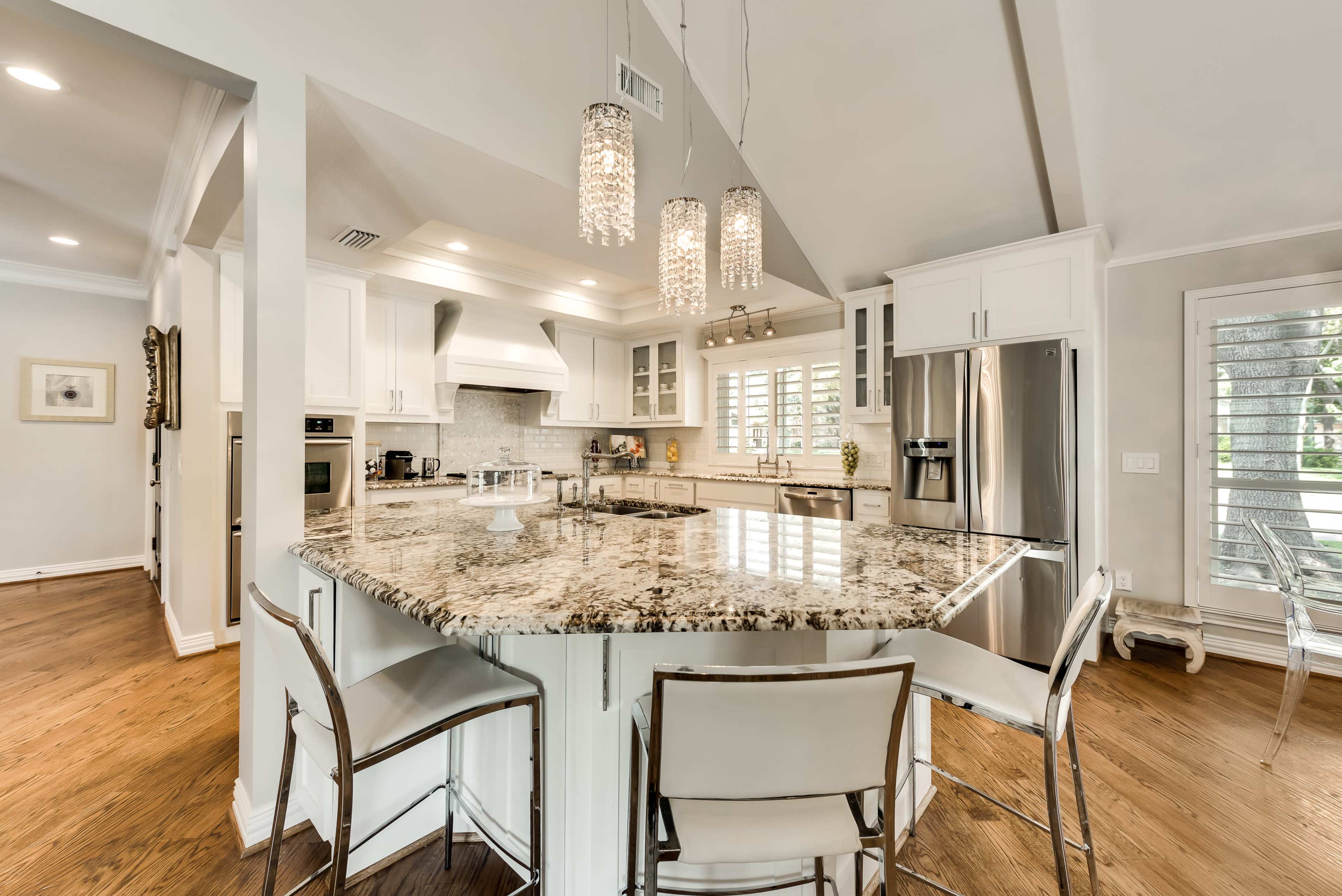 The image shows a modern kitchen with a large granite island, white cabinetry, and pendant lighting.