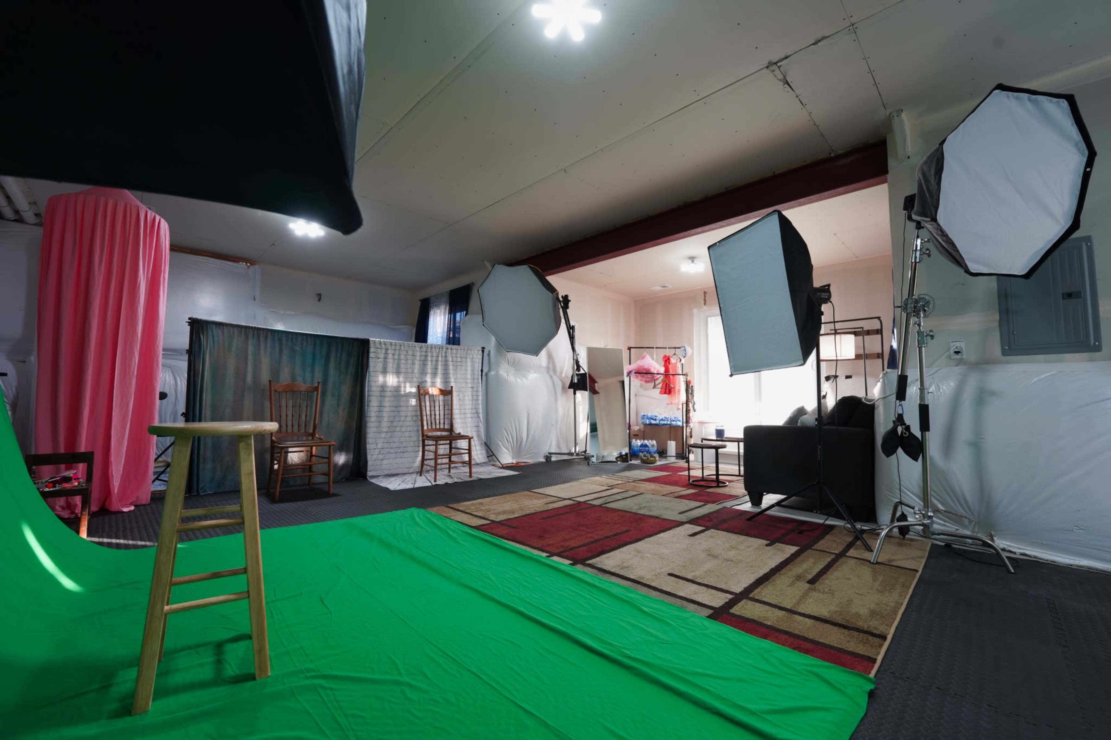 The image shows a photography studio featuring green and pink backdrops, professional lighting equipment, and various chairs arranged within the space.