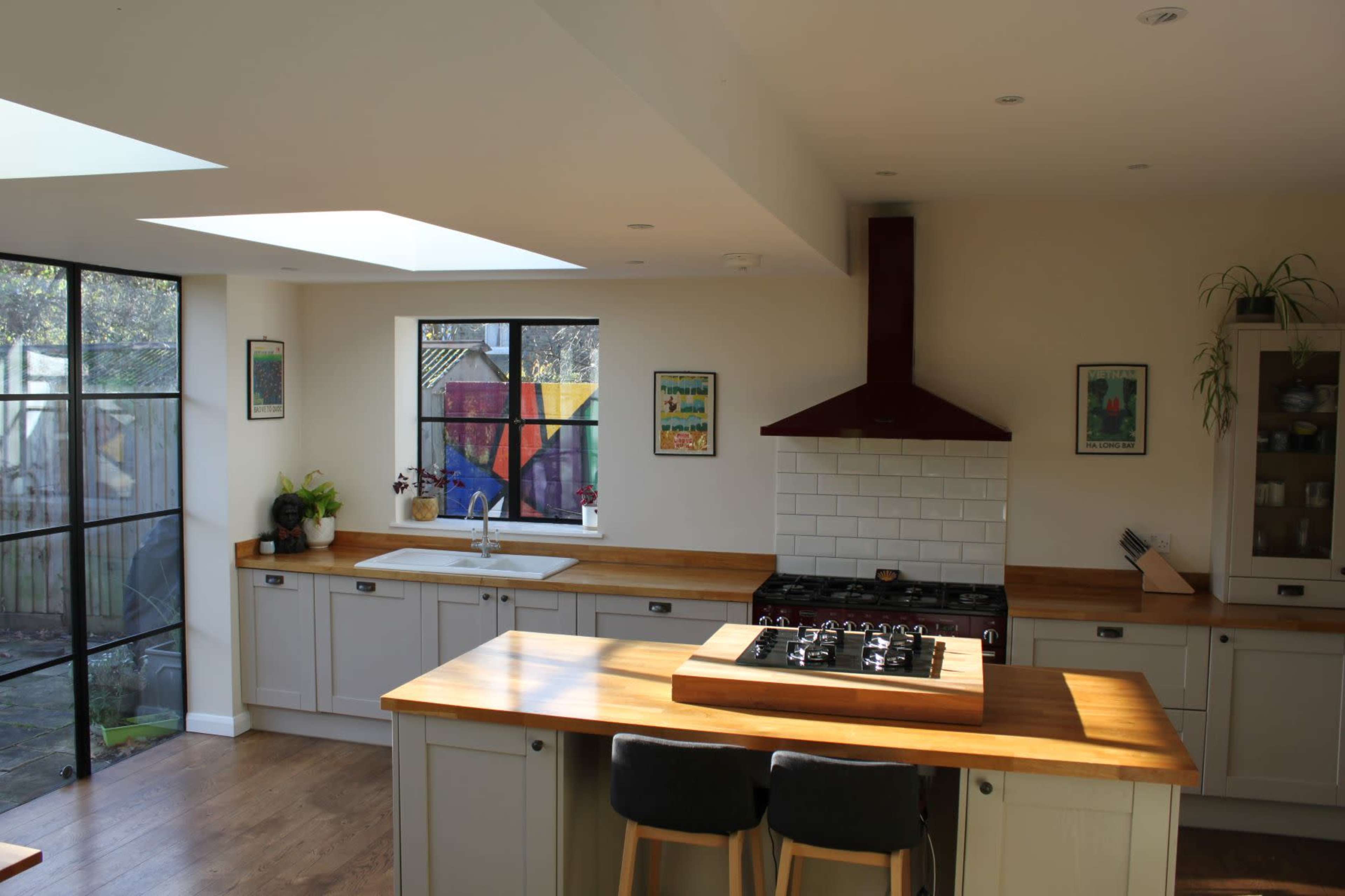 A modern kitchen with a central wooden island, a gas stove, and large windows allowing natural light to enter.