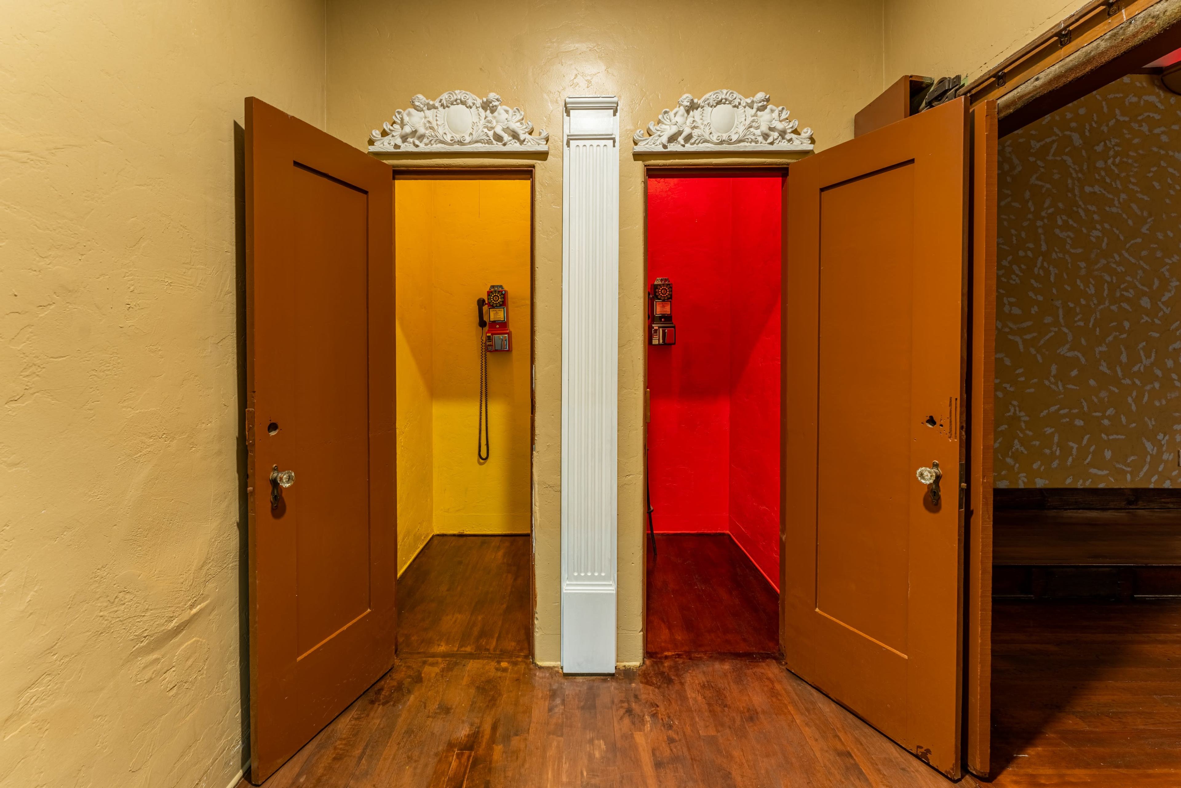 Two phone booths, one painted yellow and the other red, positioned opposite each other in a hallway with decorated walls.