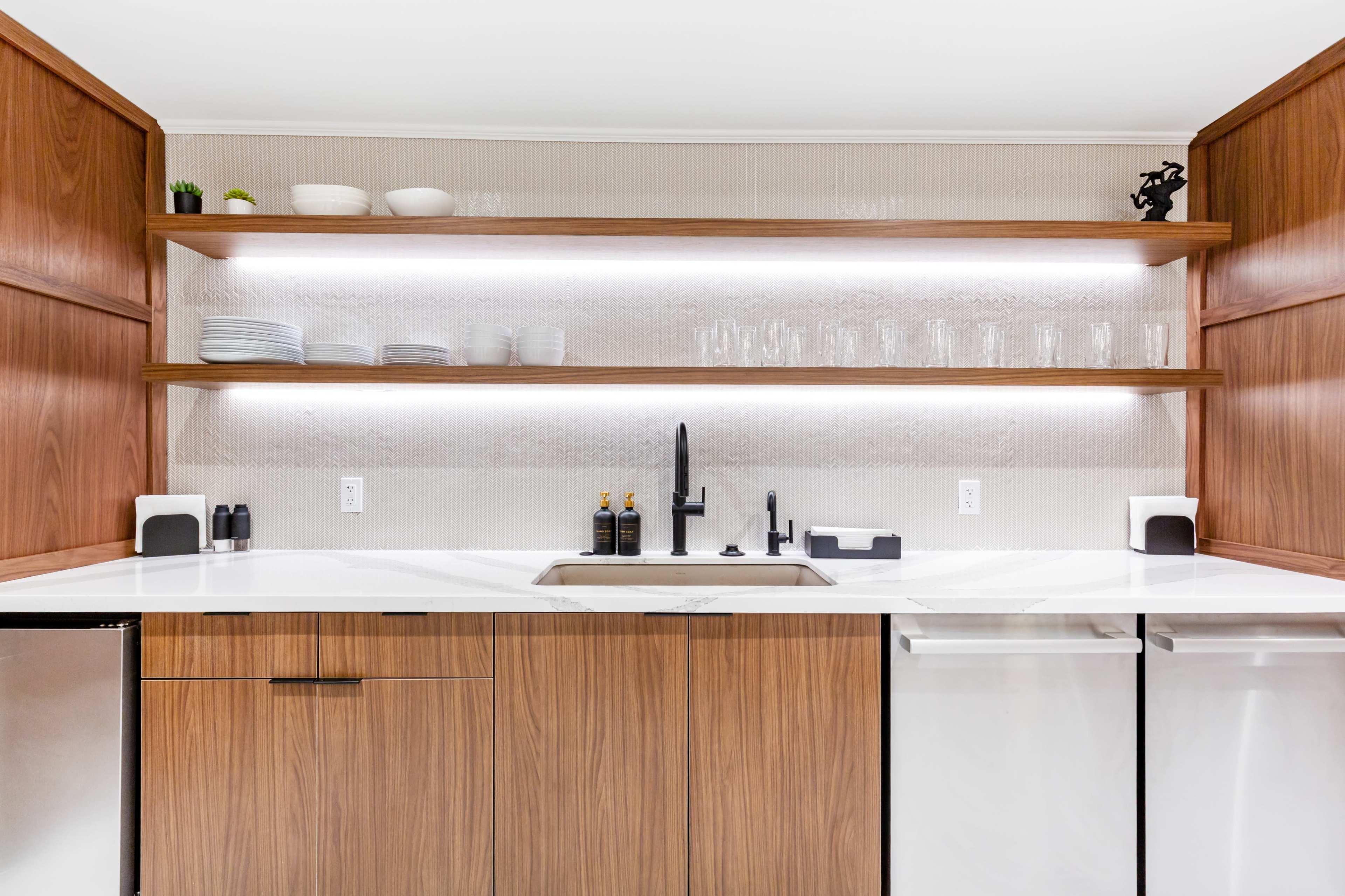 The image shows a modern kitchen with wooden cabinetry, open shelves displaying dishes, and a sleek sink area with black fixtures.