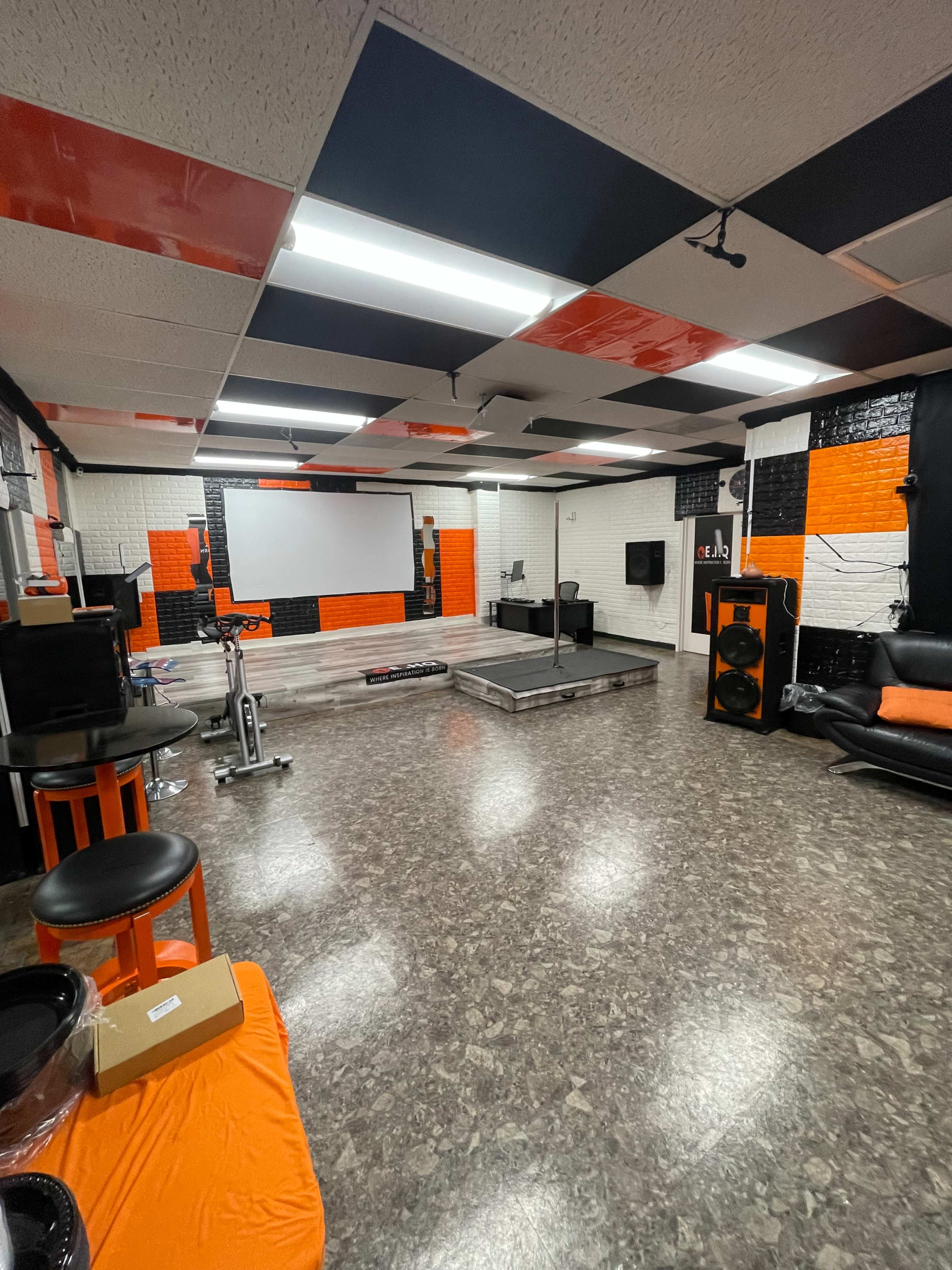A spacious entertainment room with a stage, a large projector screen, and black and orange decor.