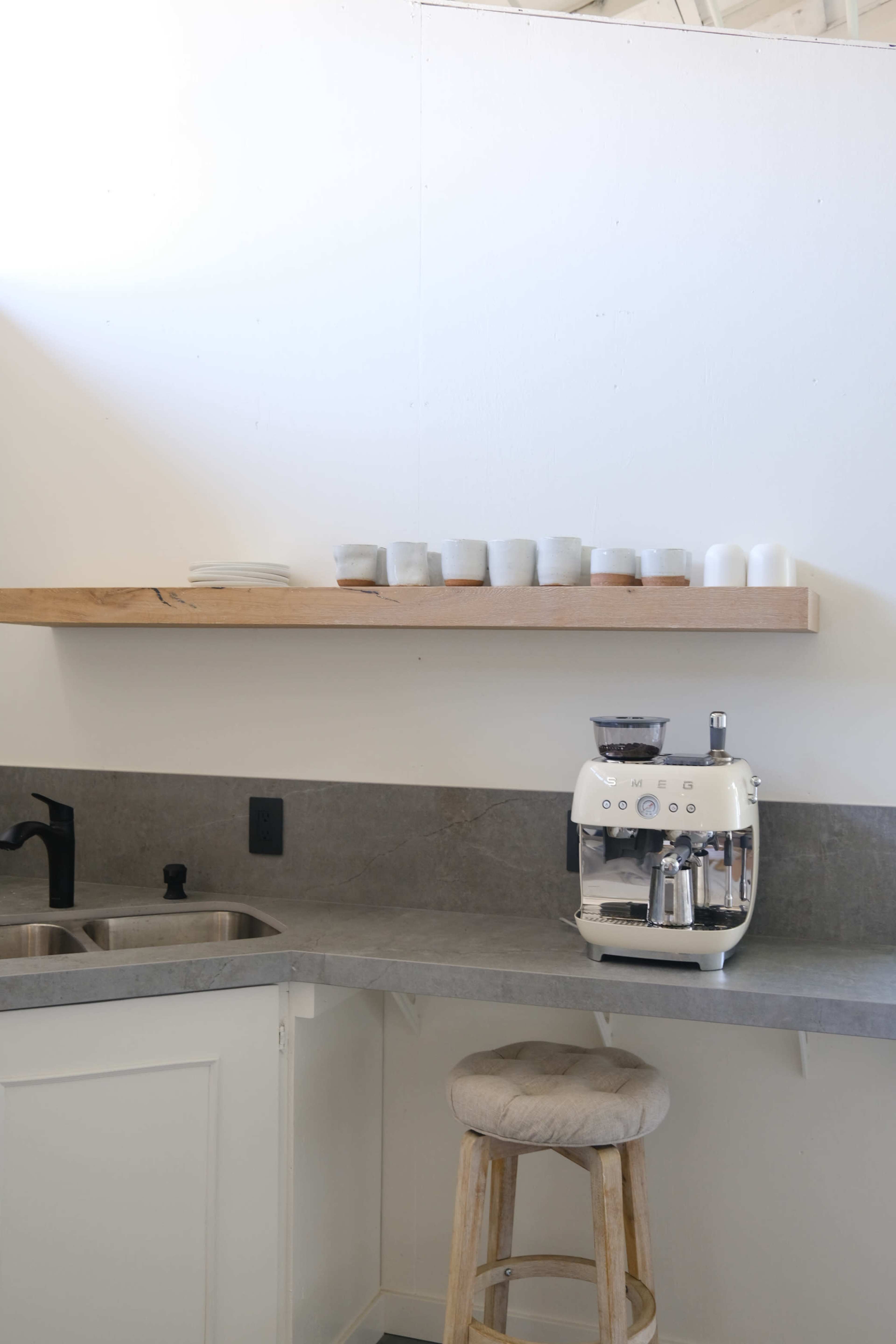 A modern kitchen features a gray countertop, a white espresso machine, and a wooden shelf displaying small cups.