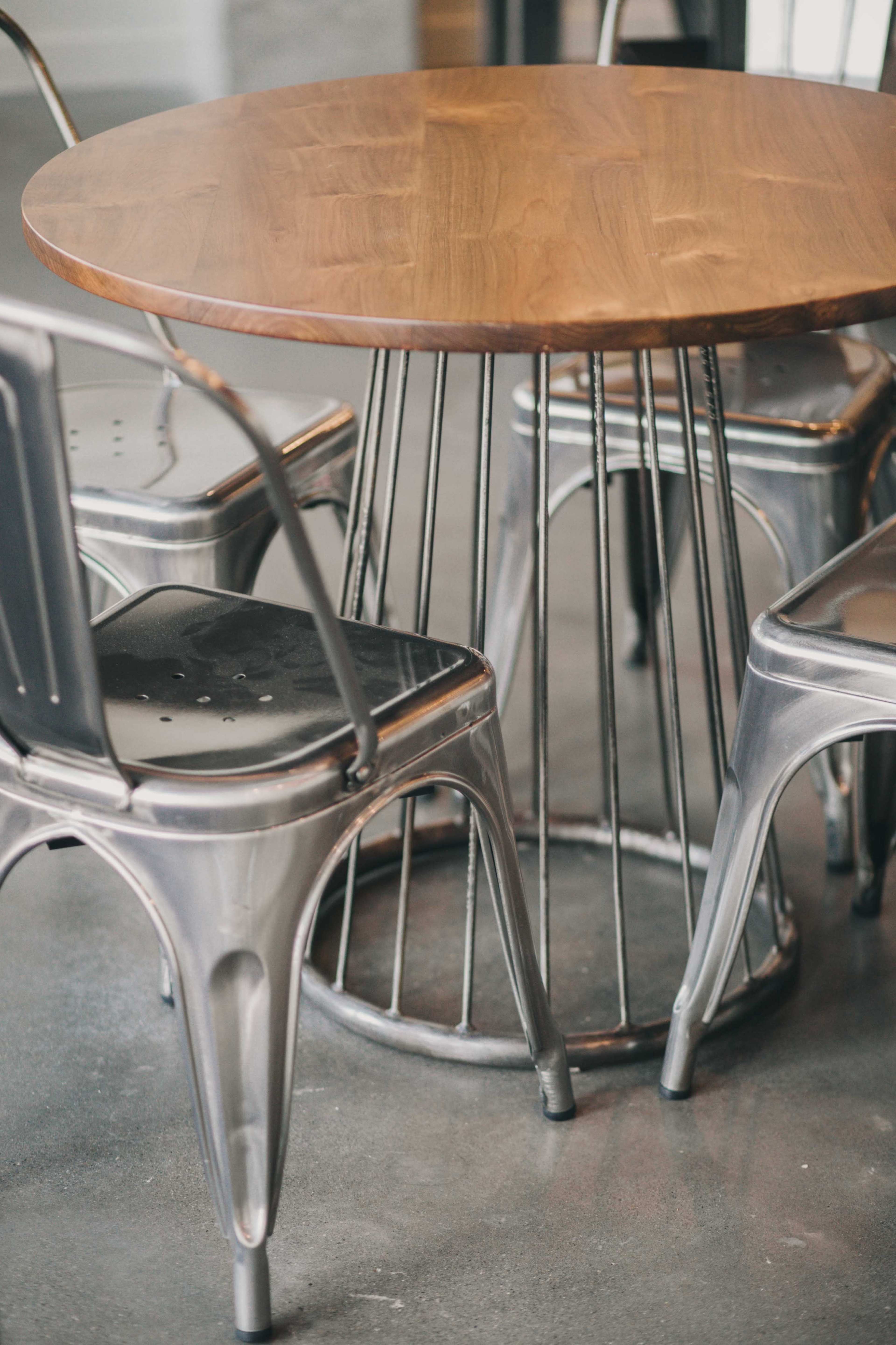 A round wooden table surrounded by four metal chairs with a minimalist design.