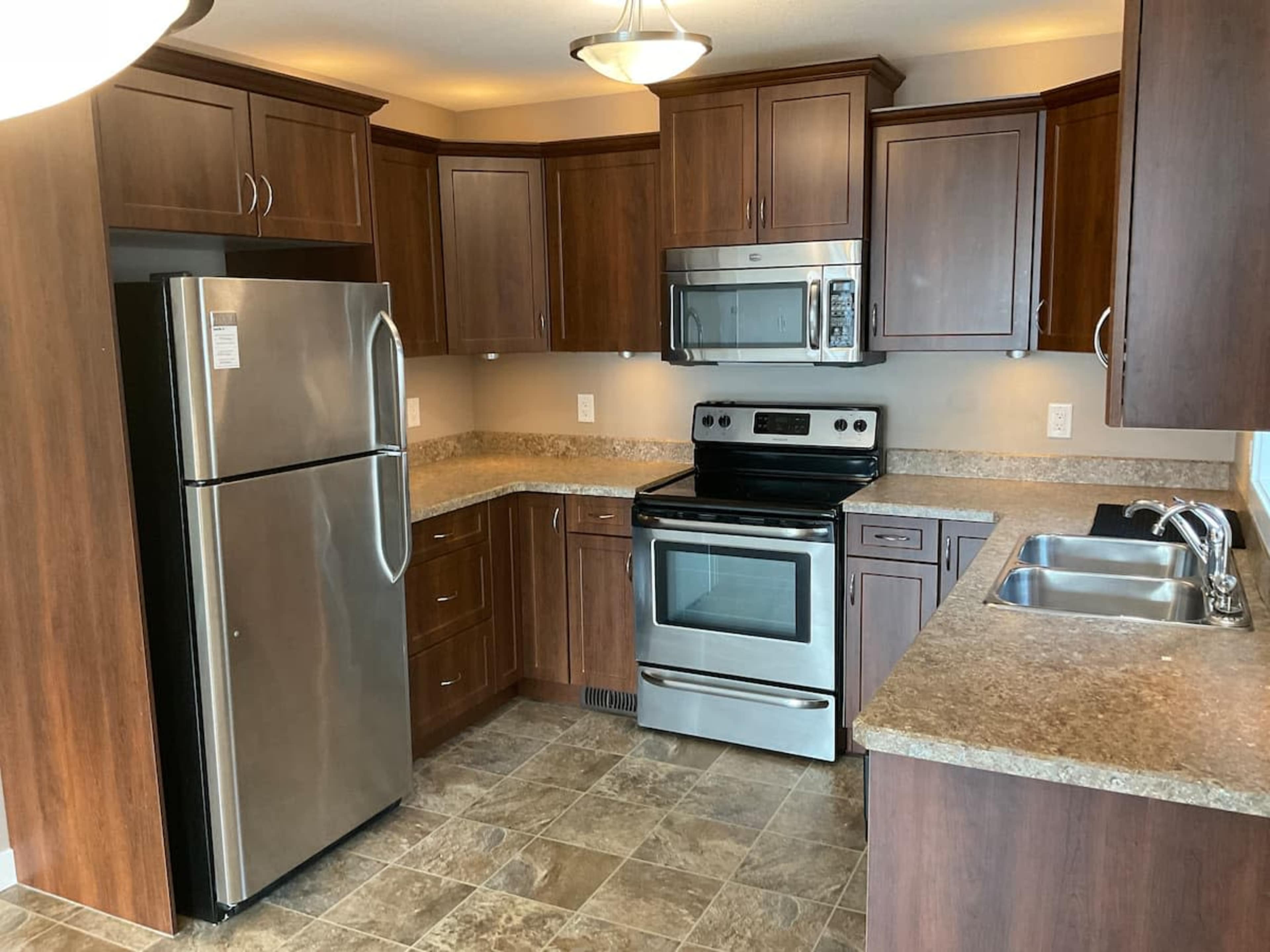 A modern kitchen with dark wooden cabinets, stainless steel appliances, and a countertop made of a light-colored material.