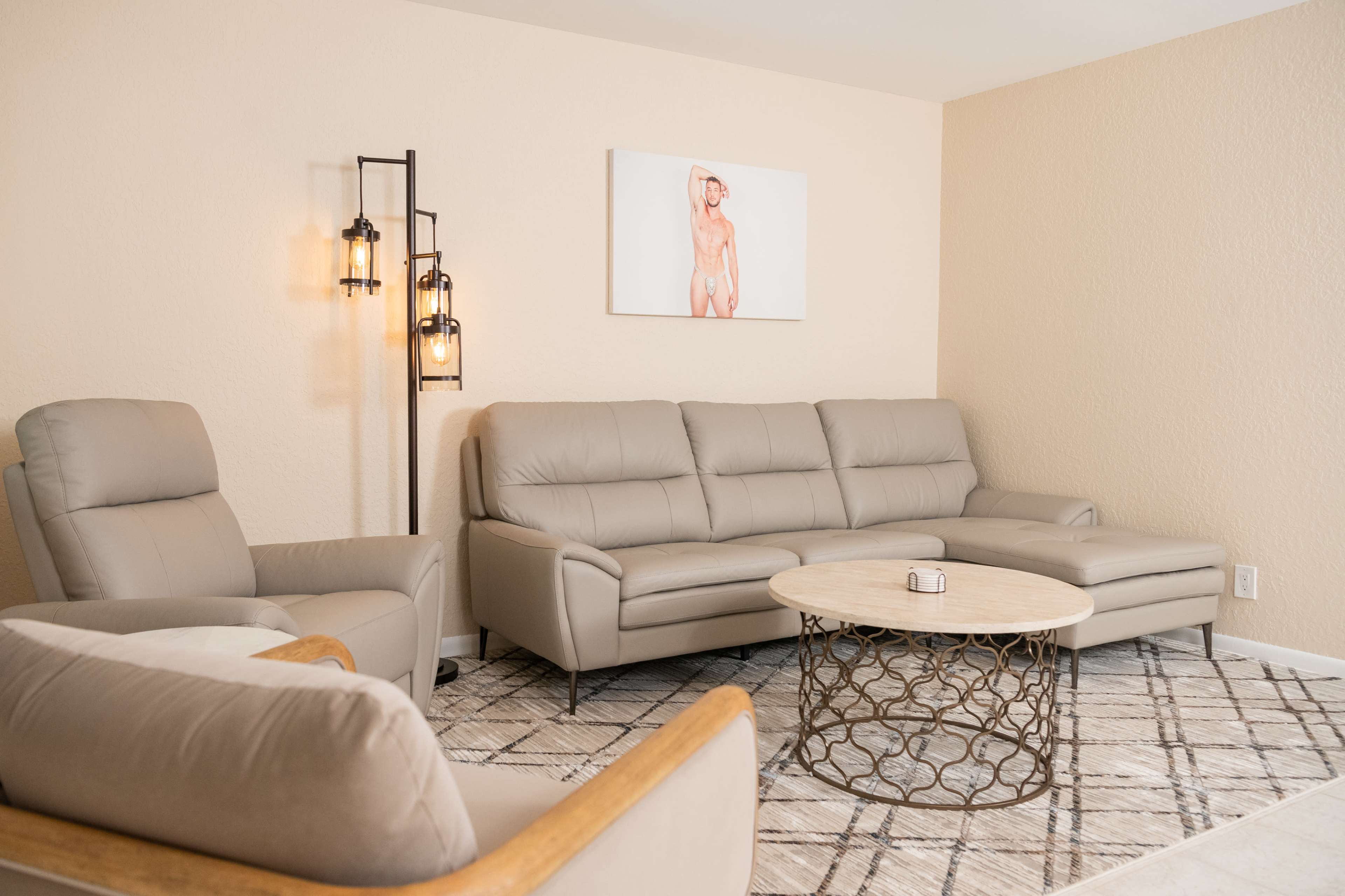A modern living room features a light gray sectional sofa, a round coffee table, and an armchair, with a decorative wall lamp and artwork in the background.