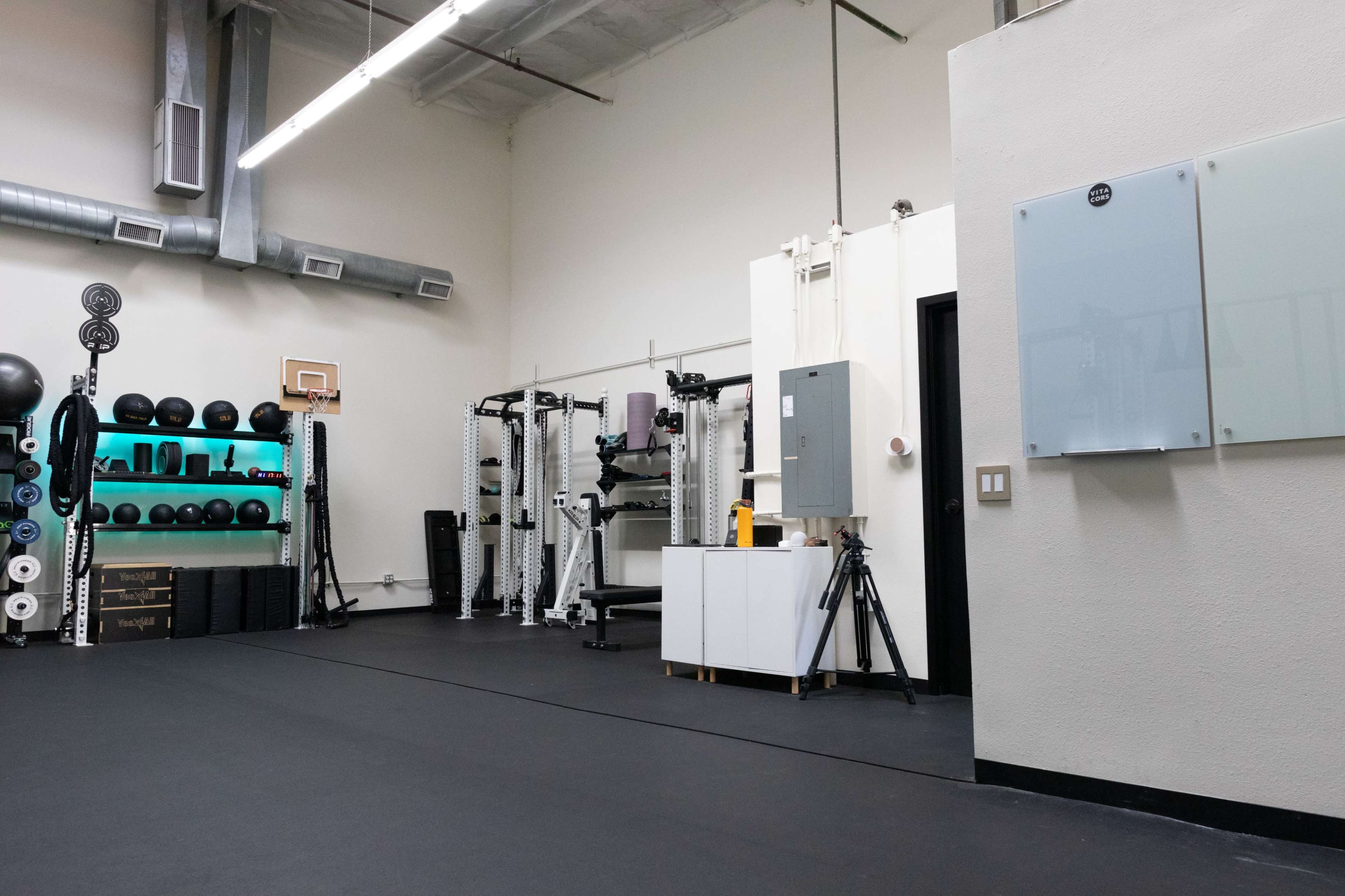 A gym interior equipped with various fitness equipment, including weights, exercise machines, and a basketball hoop.