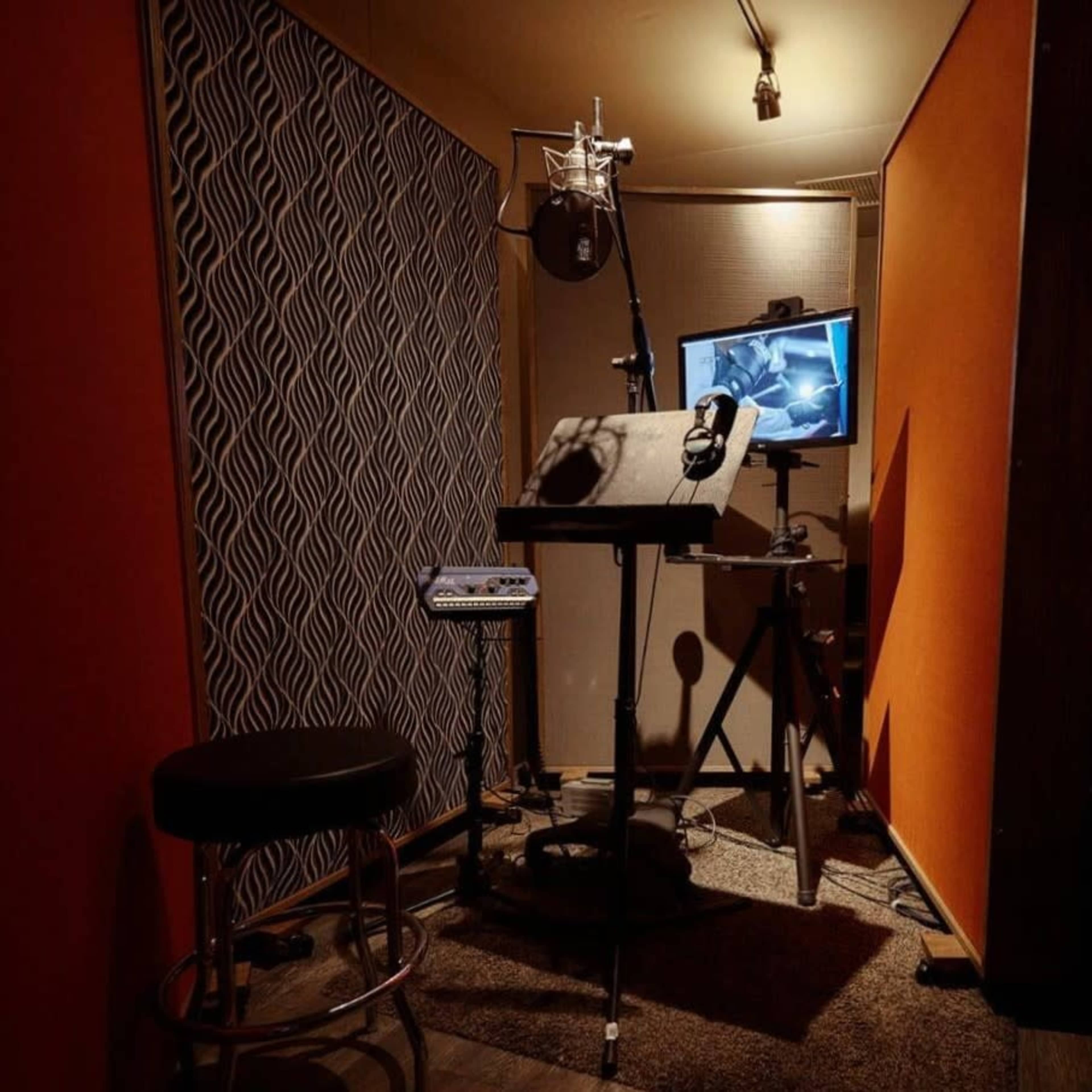 The image shows a sound recording booth with a microphone, headphones, and a monitor displaying audio software.
