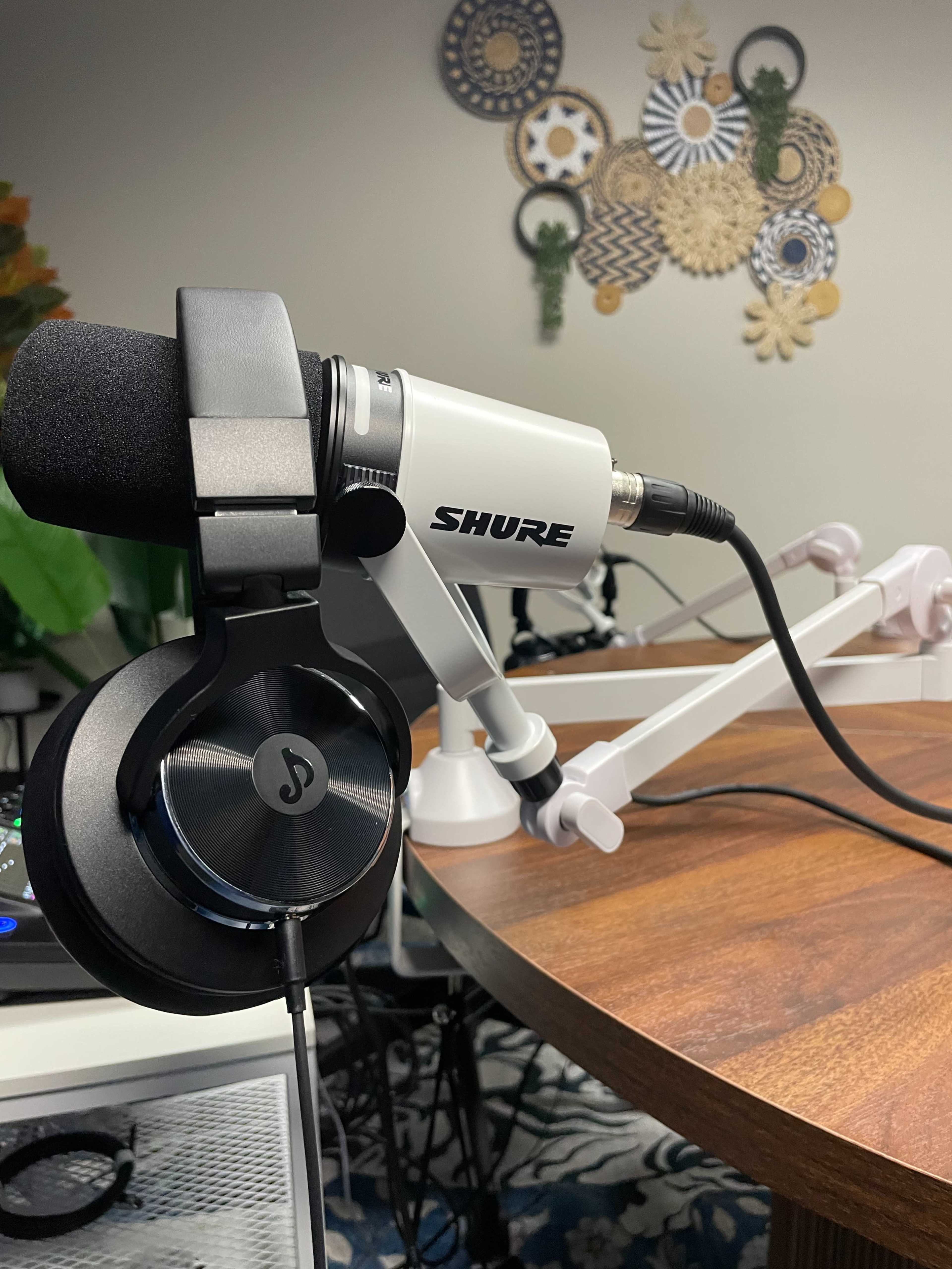 A Shure microphone is mounted on an adjustable arm next to a pair of black headphones on a wooden table.
